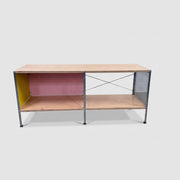 Herman Miller Eames Storage Unit featuring a low rectangular frame with plywood shelves, a yellow side panel, a pink back panel, and a perforated metal side.