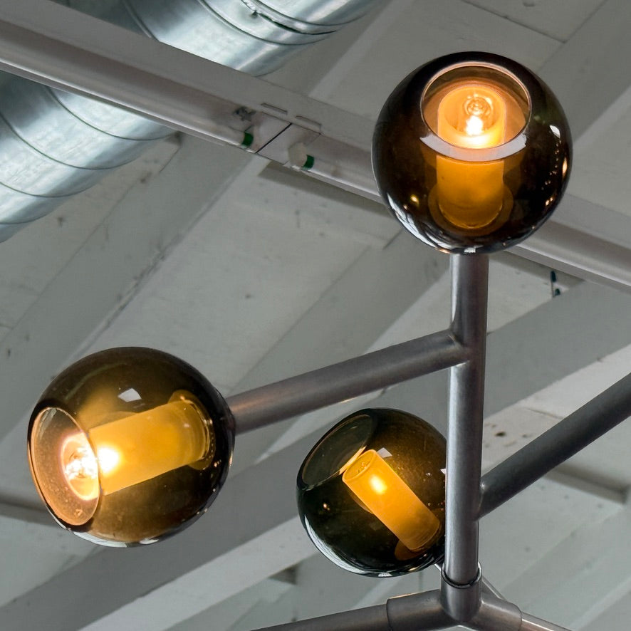The Pouenat Last Night Branche Chandelier by Pouenat, featuring mouth-blown glass spheres, hangs beneath a white exposed beam ceiling with visible ductwork—an ideal statement for modern industrial interiors.