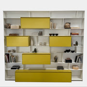 Close-up of a yellow cabinet door with a small paint chip on the bottom edge; black bowls and books are seen on a white shelf of the B&B Italia Flat C Wall Unit With Storage by B&B Italia, combining style and function.