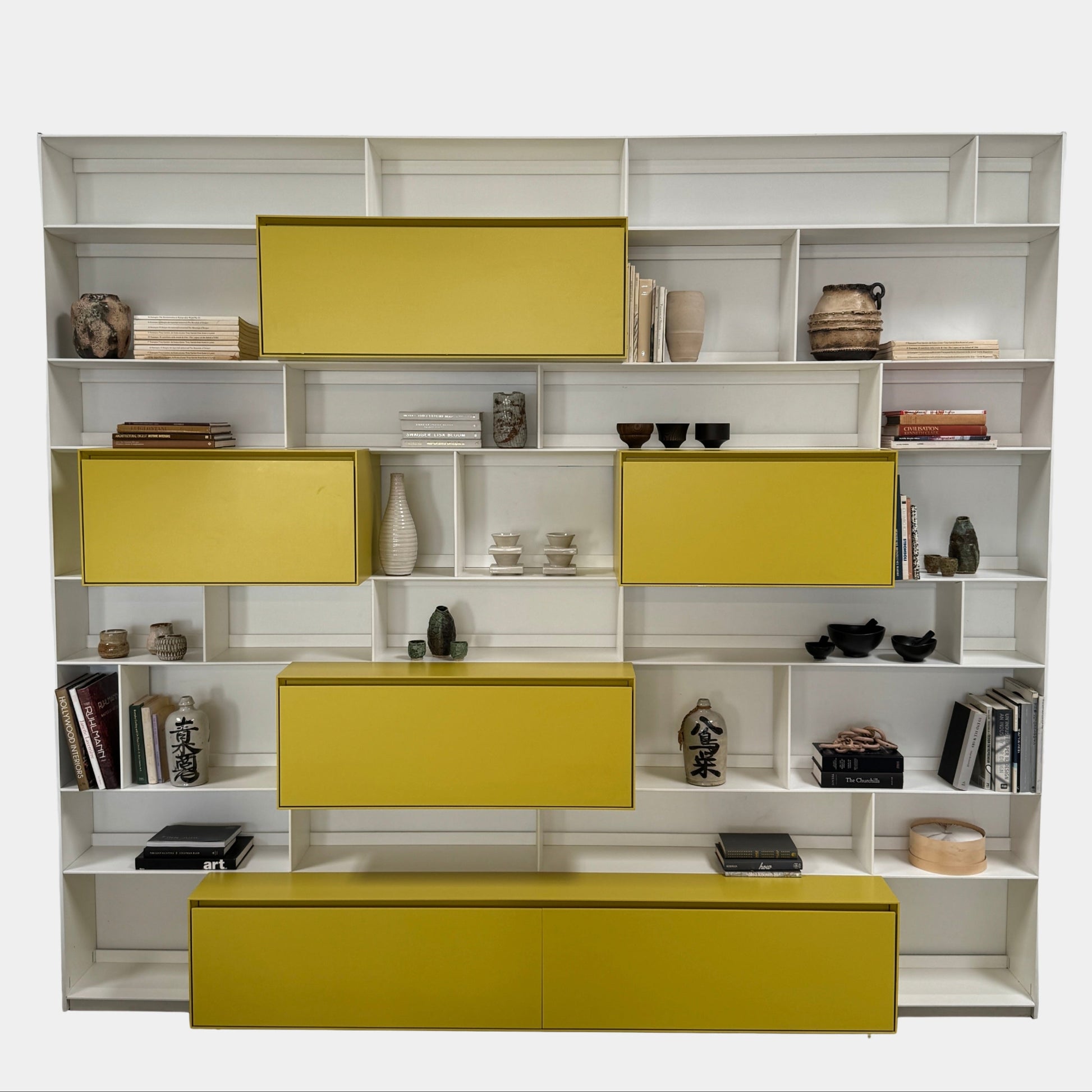 Close-up of a yellow cabinet door with a small paint chip on the bottom edge; black bowls and books are seen on a white shelf of the B&B Italia Flat C Wall Unit With Storage by B&B Italia, combining style and function.