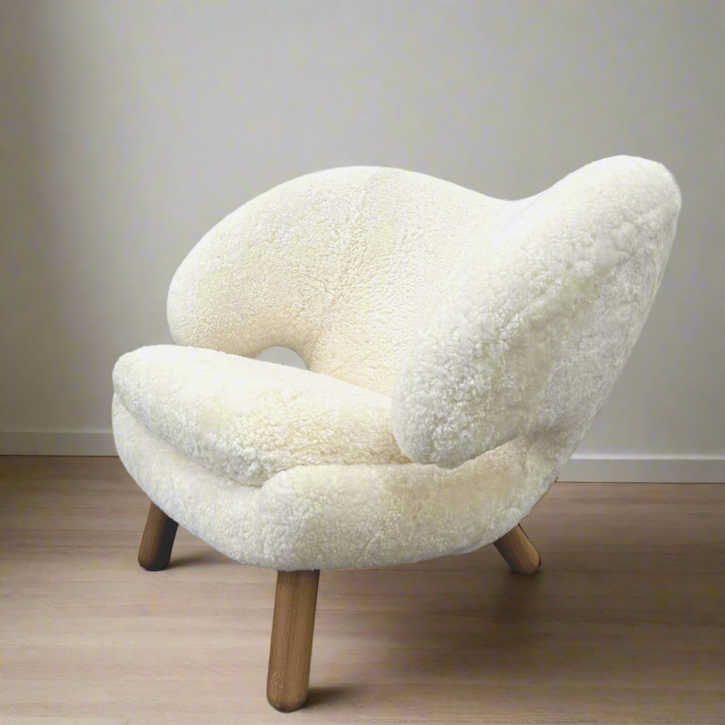 The House of Finn Juhl Finn Juhl Pelican Chair Sheepskin, with curved armrests and wooden legs, is displayed against a plain white background.