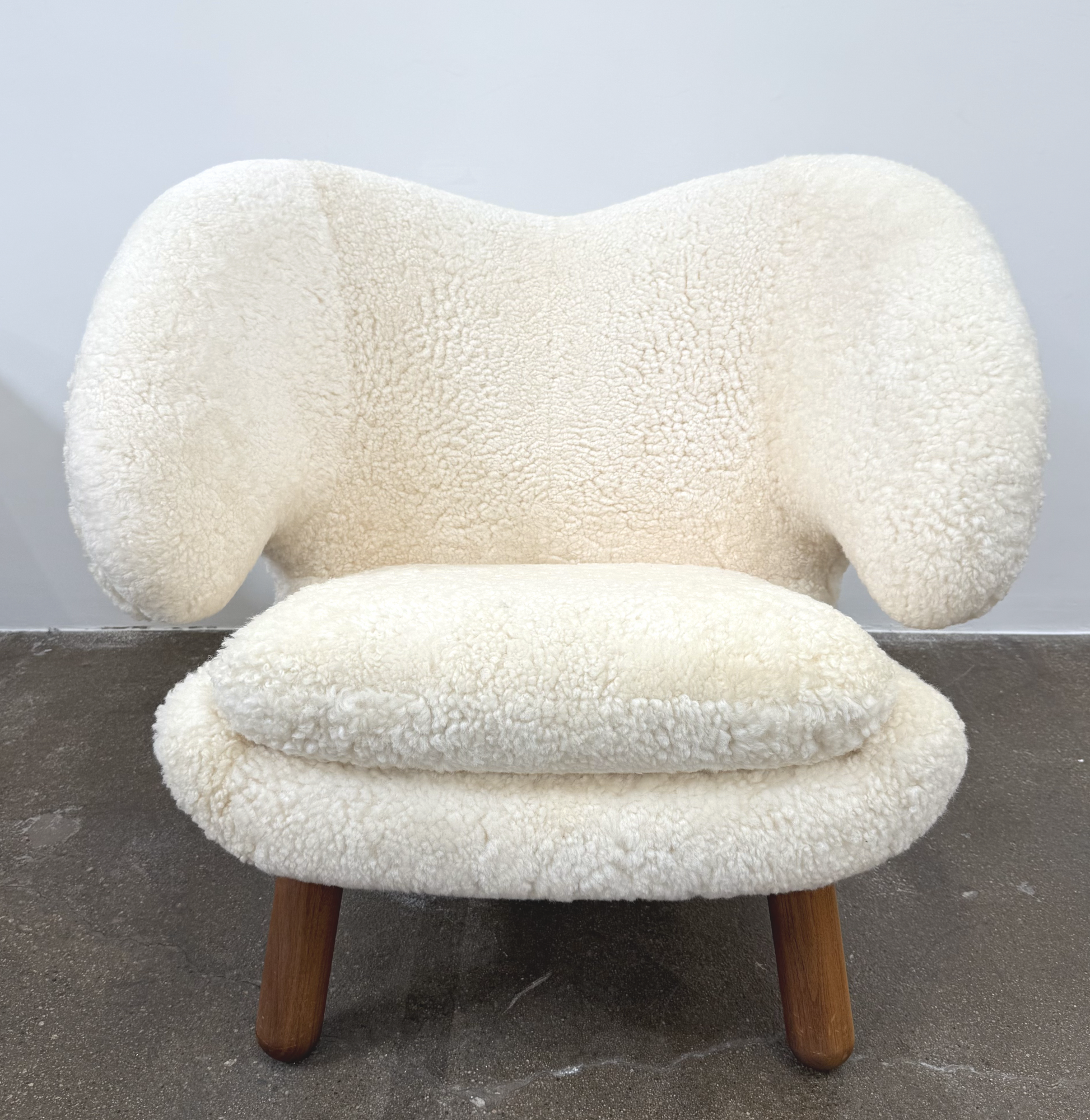 The House of Finn Juhl Finn Juhl Pelican Chair Sheepskin, with curved armrests and wooden legs, is displayed against a plain white background.
