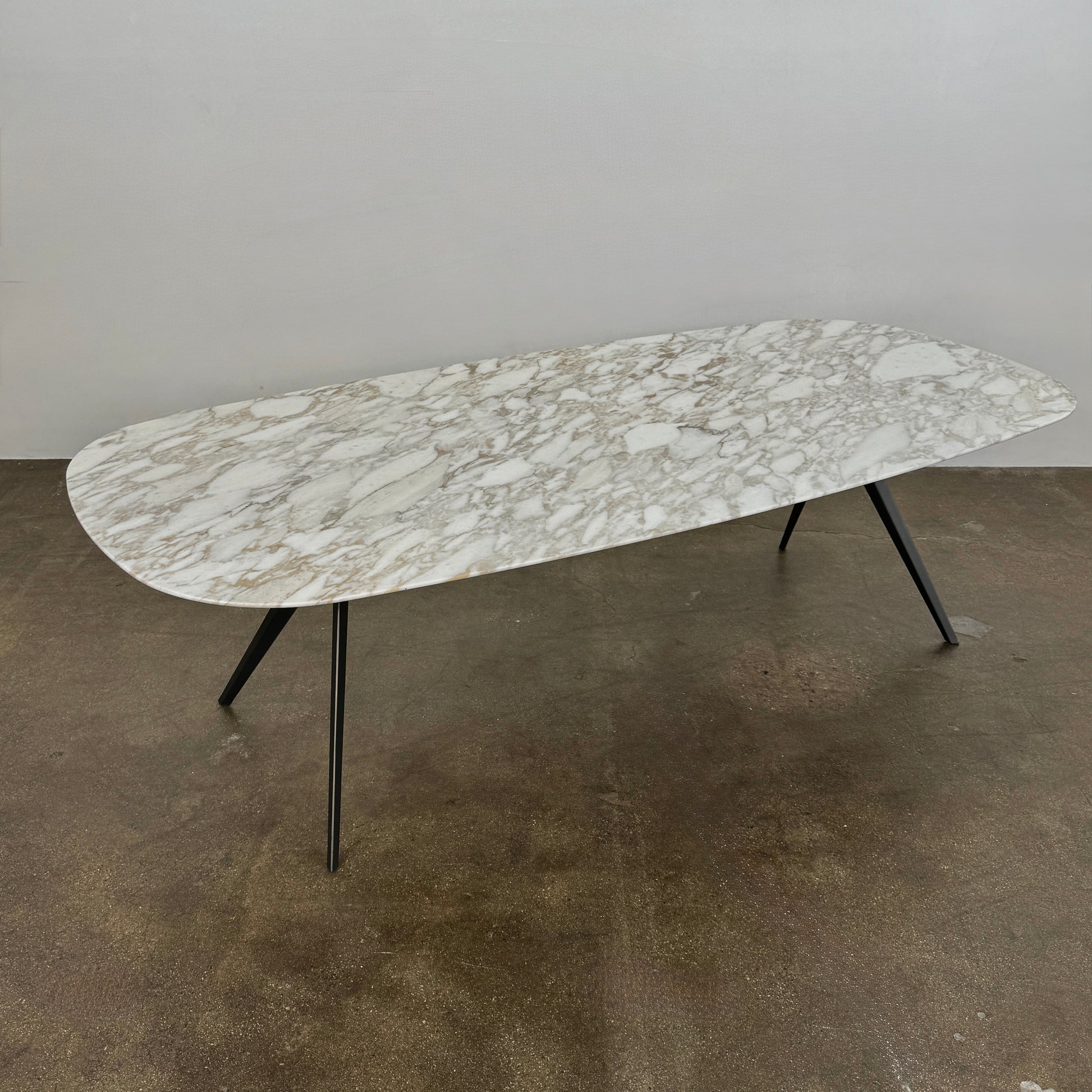 The Flexform Zefiro Dining Table by Flexform features a rectangular Calacatta Gold marble top with rounded edges and four black angled legs, shown on a plain white background.