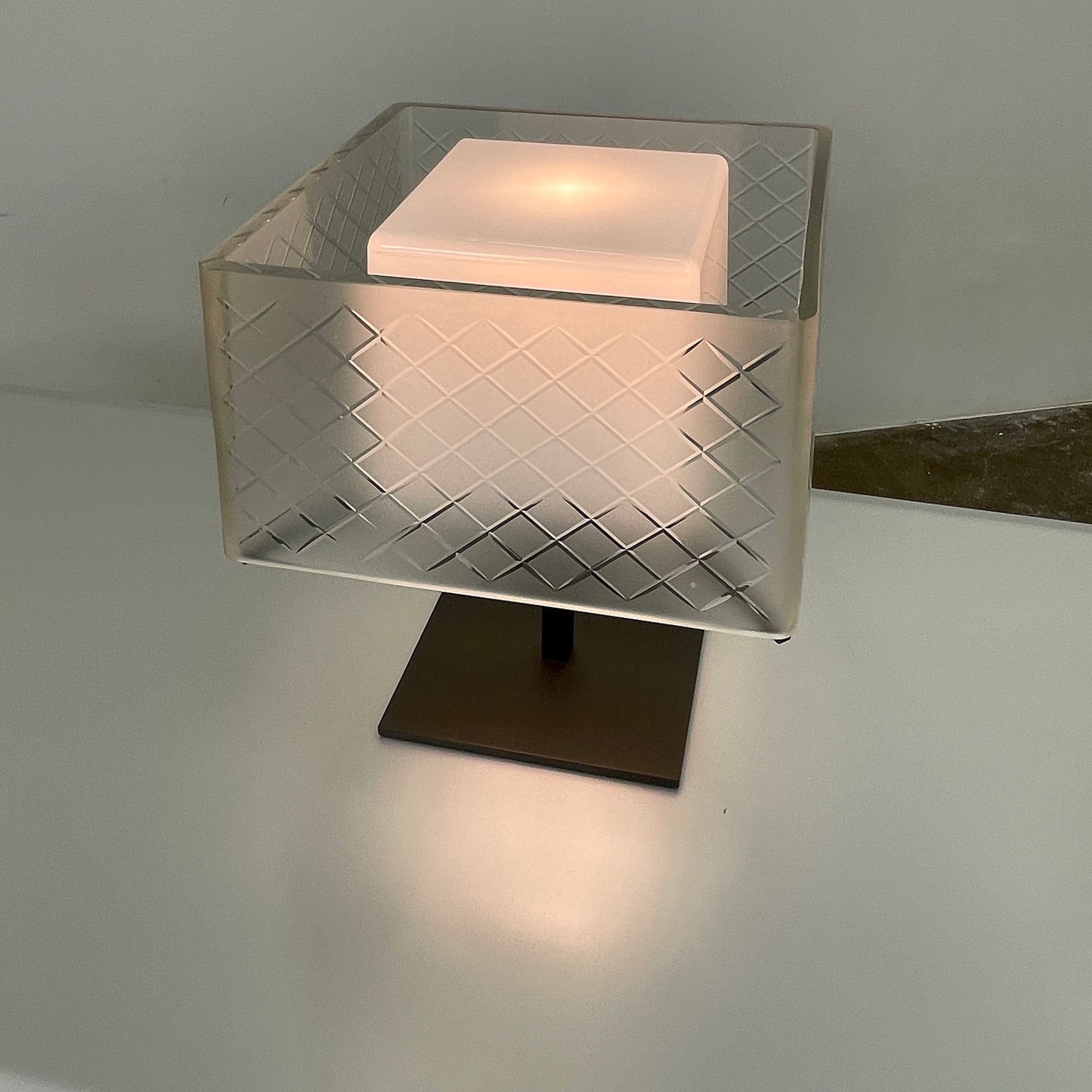 Introducing the Flos Metropolitan Table Light by Flos: a chic table lamp with a rectangular shade adorned with a diamond pattern, gracefully positioned on a square base.