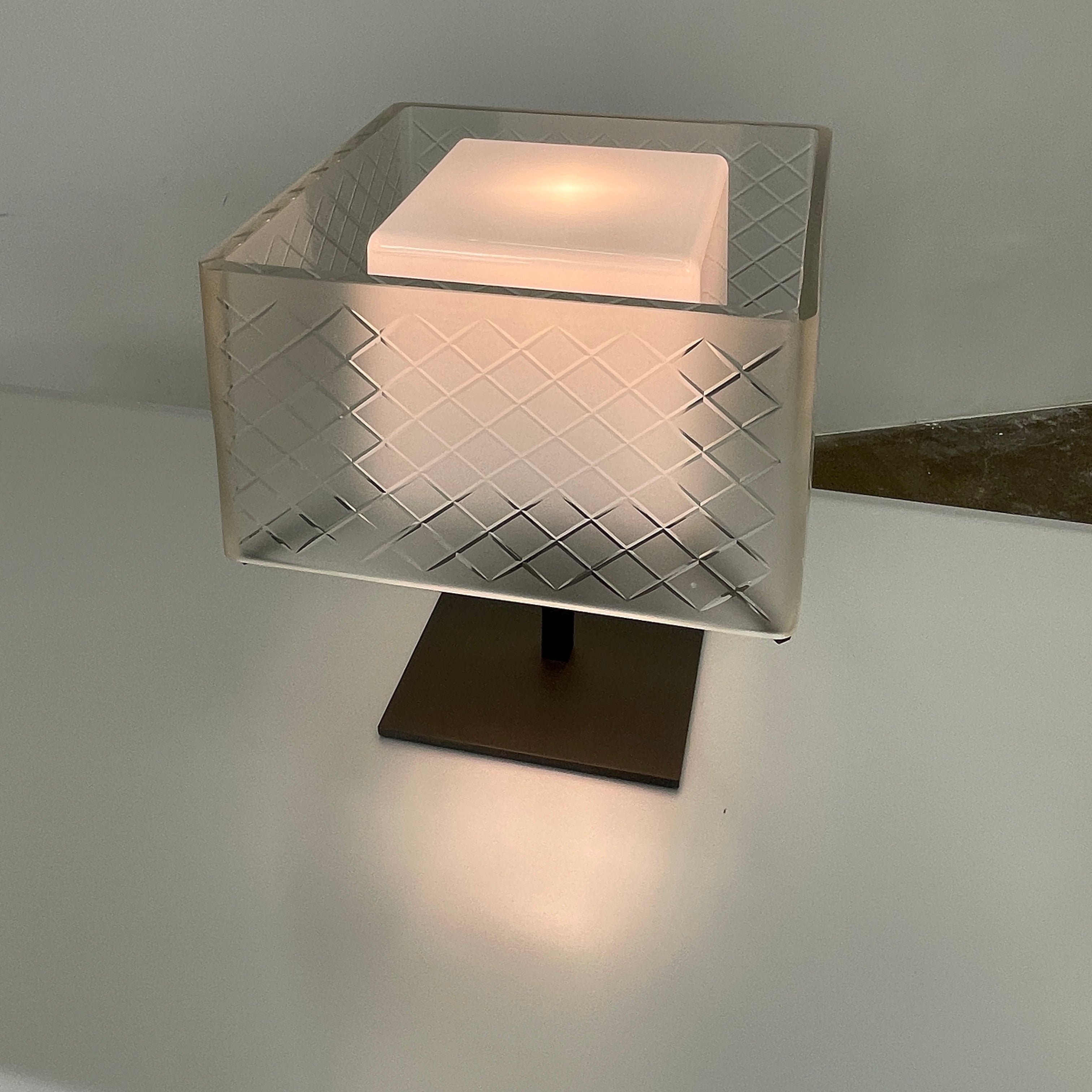 Introducing the Flos Metropolitan Table Light by Flos: a chic table lamp with a rectangular shade adorned with a diamond pattern, gracefully positioned on a square base.