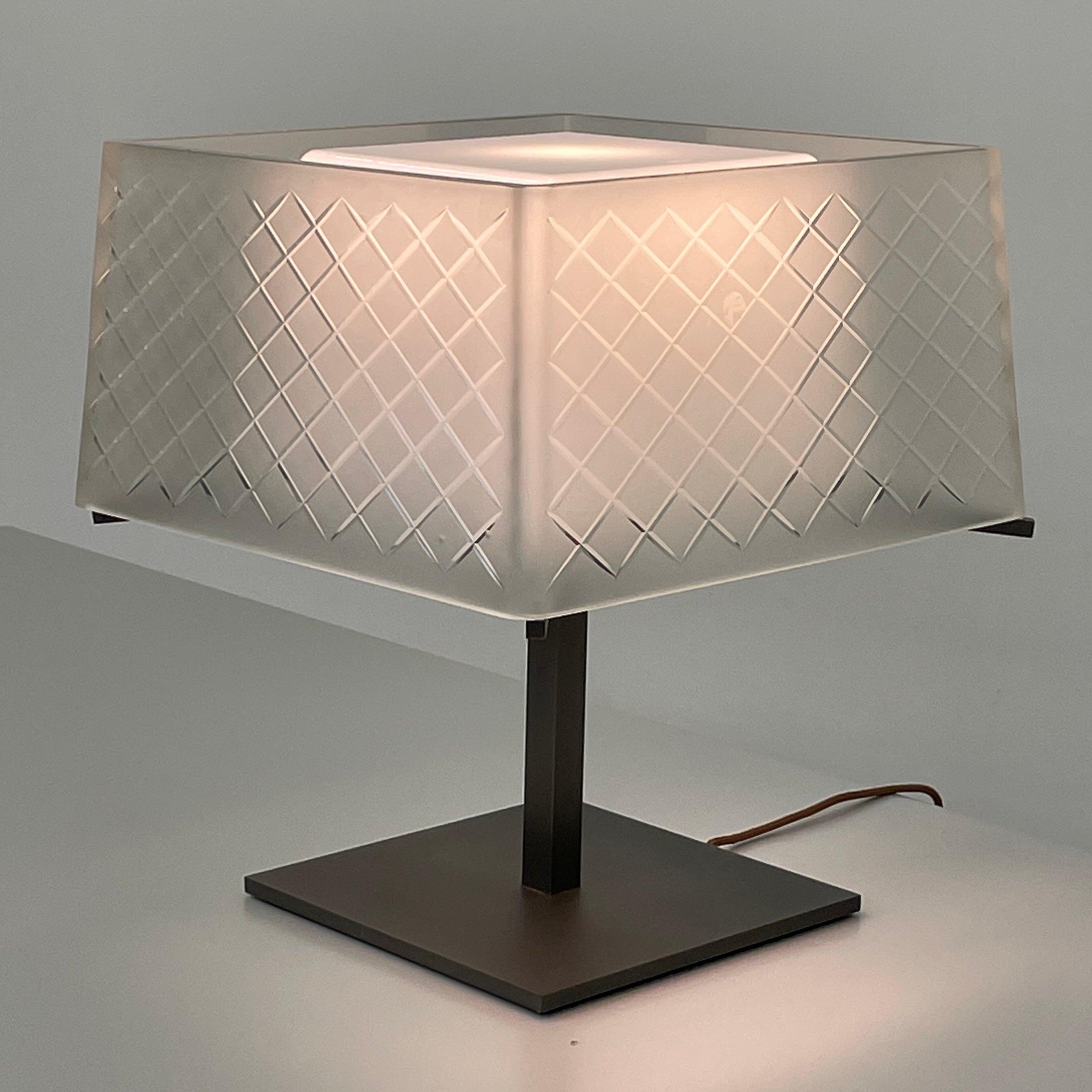 Introducing the Flos Metropolitan Table Light by Flos: a chic table lamp with a rectangular shade adorned with a diamond pattern, gracefully positioned on a square base.