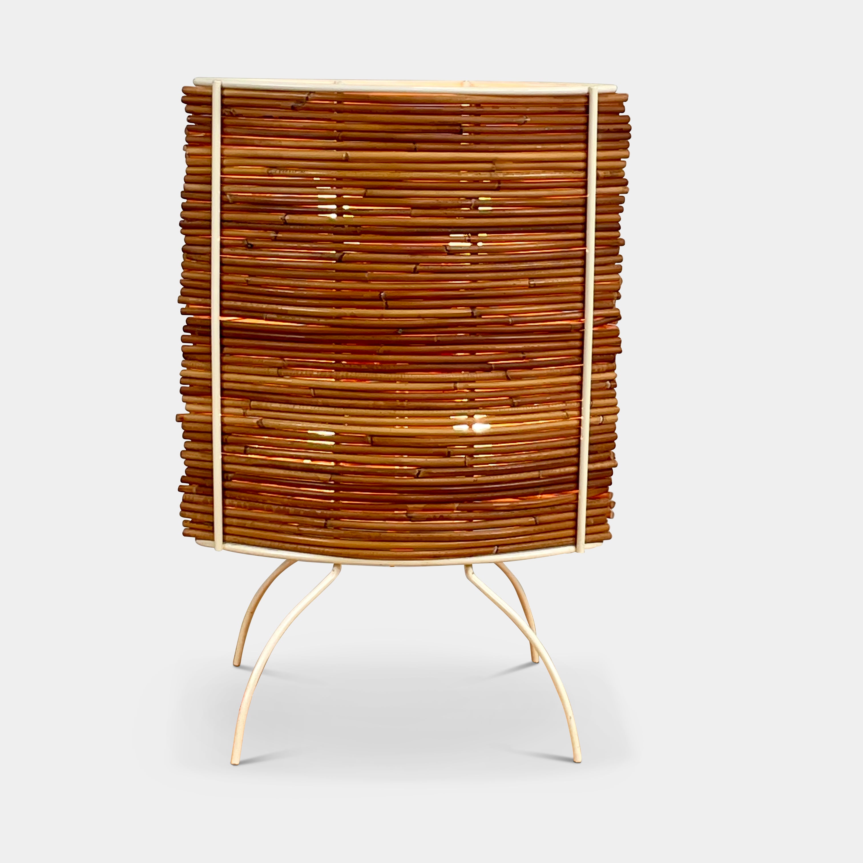 The Vintage Fontana Arte Bambú Table Light by Fontana Arte showcases a woven rattan circular shade atop a sleek white metal tripod base, making it an elegant addition to a wooden table. This lamp enhances your home's interior lighting with its natural charm and unique design.