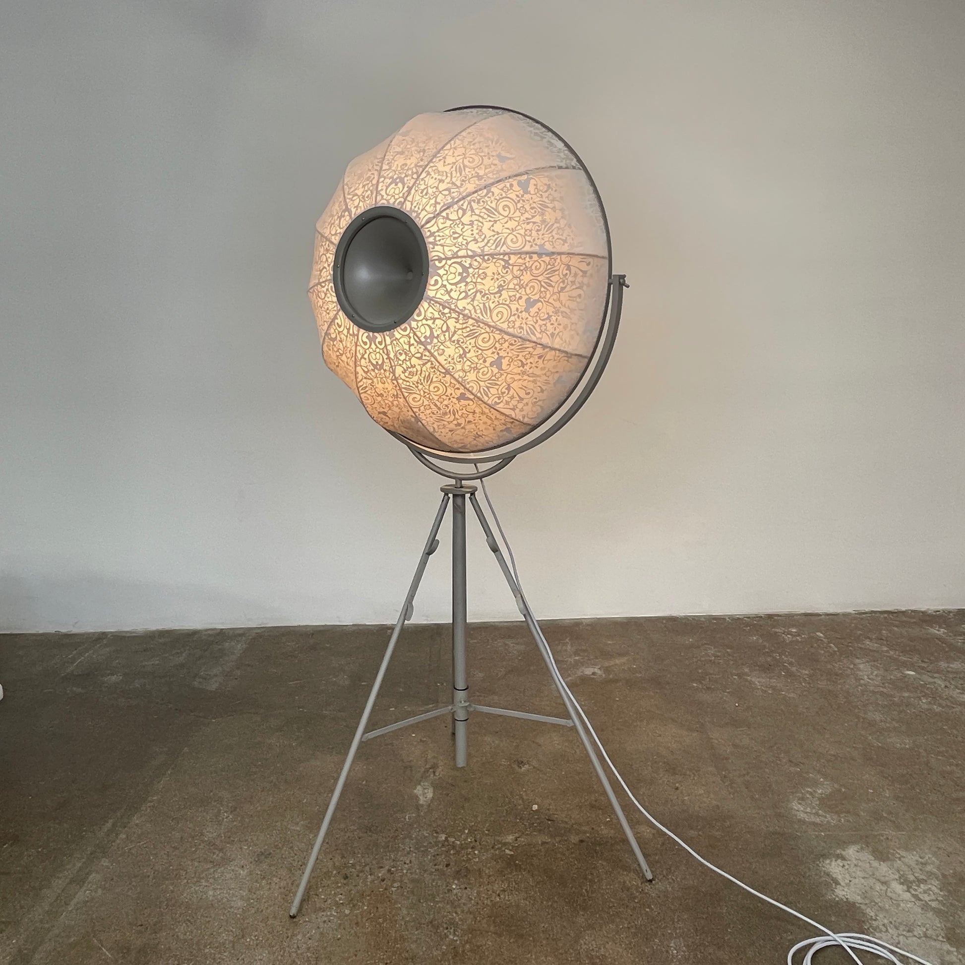 The Pallucco Italia Fortuny Ornament Floor Lamp, with its visible bulb and patterned spherical shade, gracefully stands on a plain white background, epitomizing the elegance of Pallucco Italia.