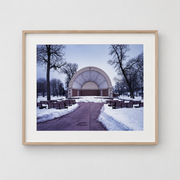 Framed Photograph - Metrostage by Cindy Bernard 2004 showing an outdoor bandshell in a snow-covered park with rows of empty benches.