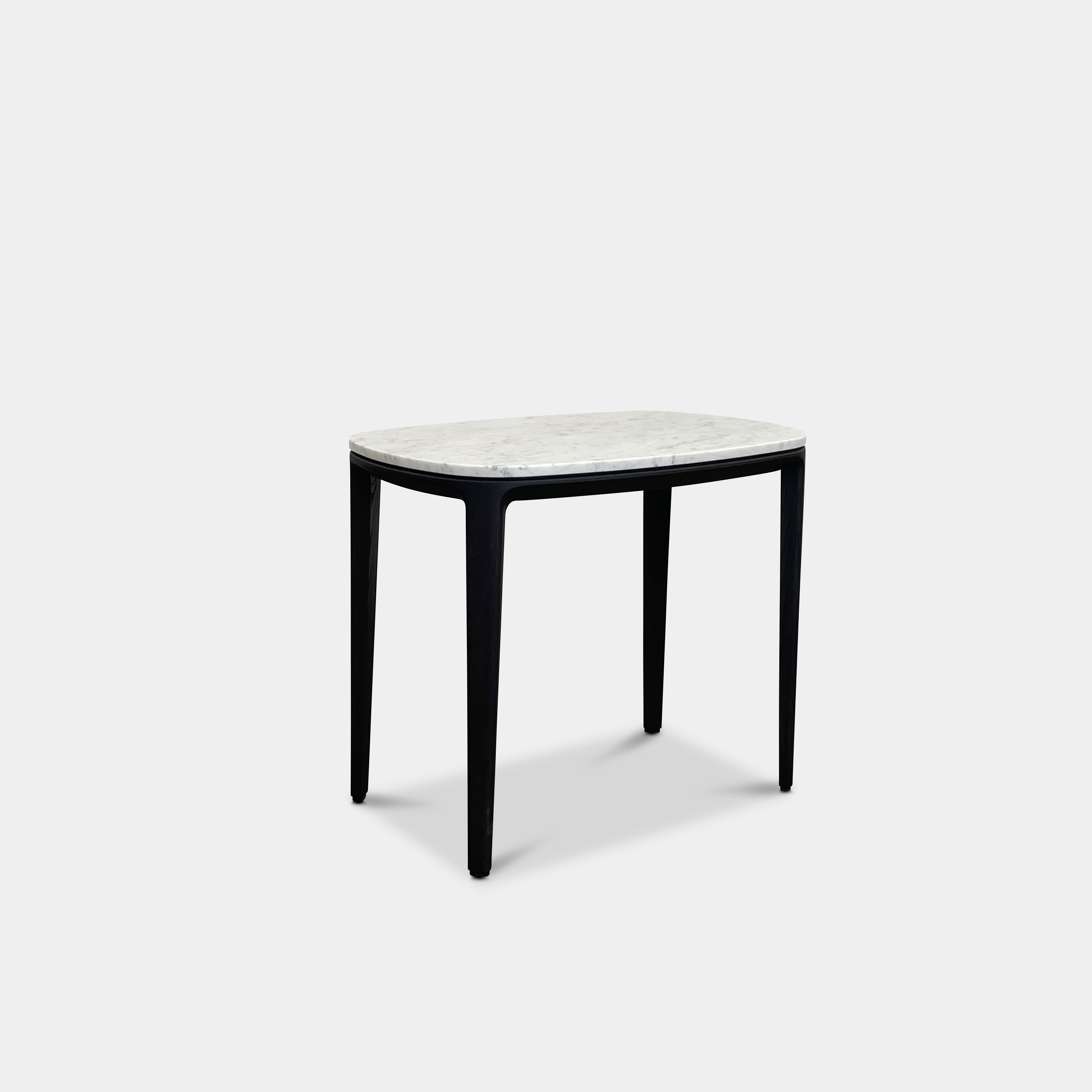 The Poliform Henry Marble Side Table, by Poliform, showcases an elegant small oval design with a luxurious Carrara marble top. It stands gracefully on four black Elm legs against a minimalist white backdrop.
