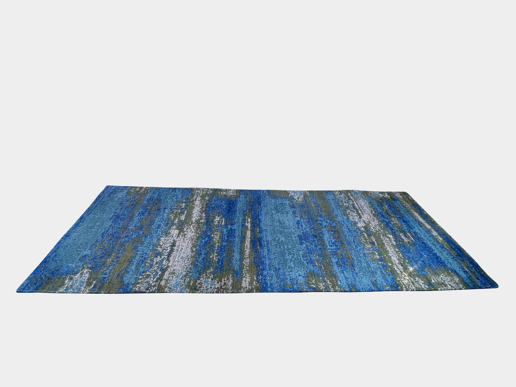 A Delinear Pixilated Rug made of pure Himalayan wool in blue and gold colors placed on a white background.