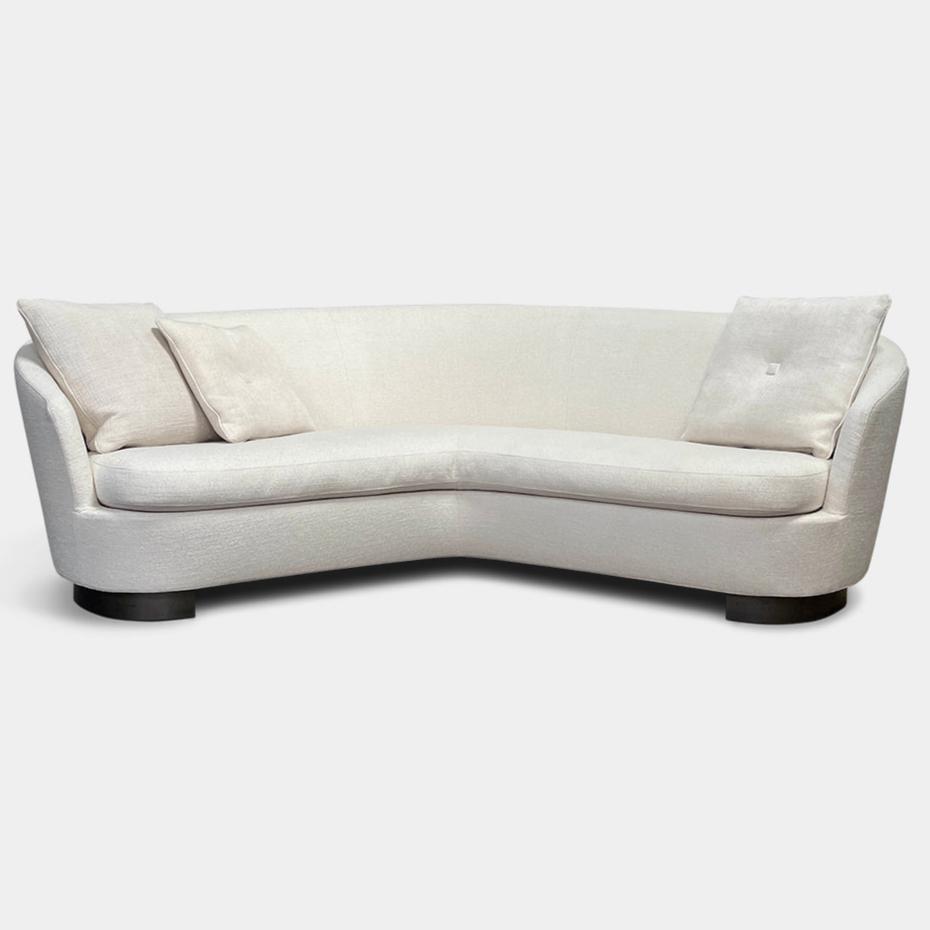 A Minotti Jacques Curved Sofa in white, featuring a contemporary design with curved lines and accompanied by two matching pillows, stands against a neutral background.