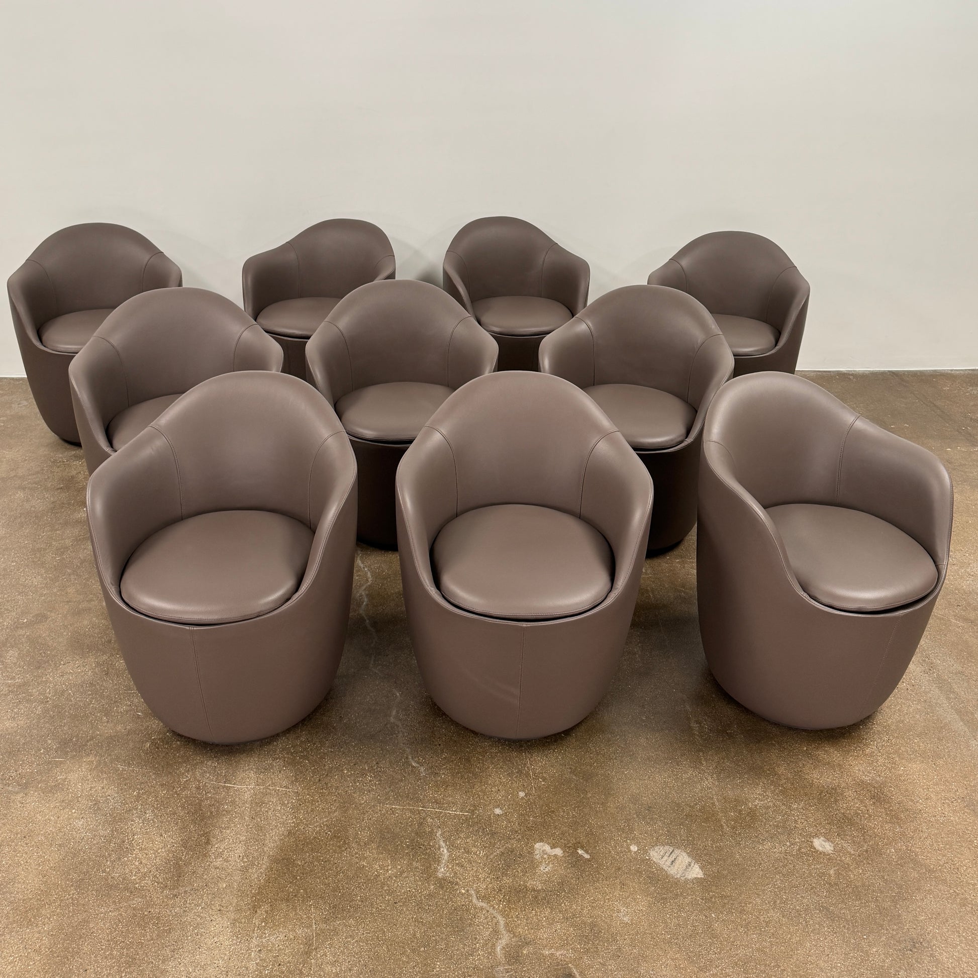 Two modern brown DWR Lina Swivel Dining Chairs with rounded backs and smooth upholstery, placed side by side on a white background.