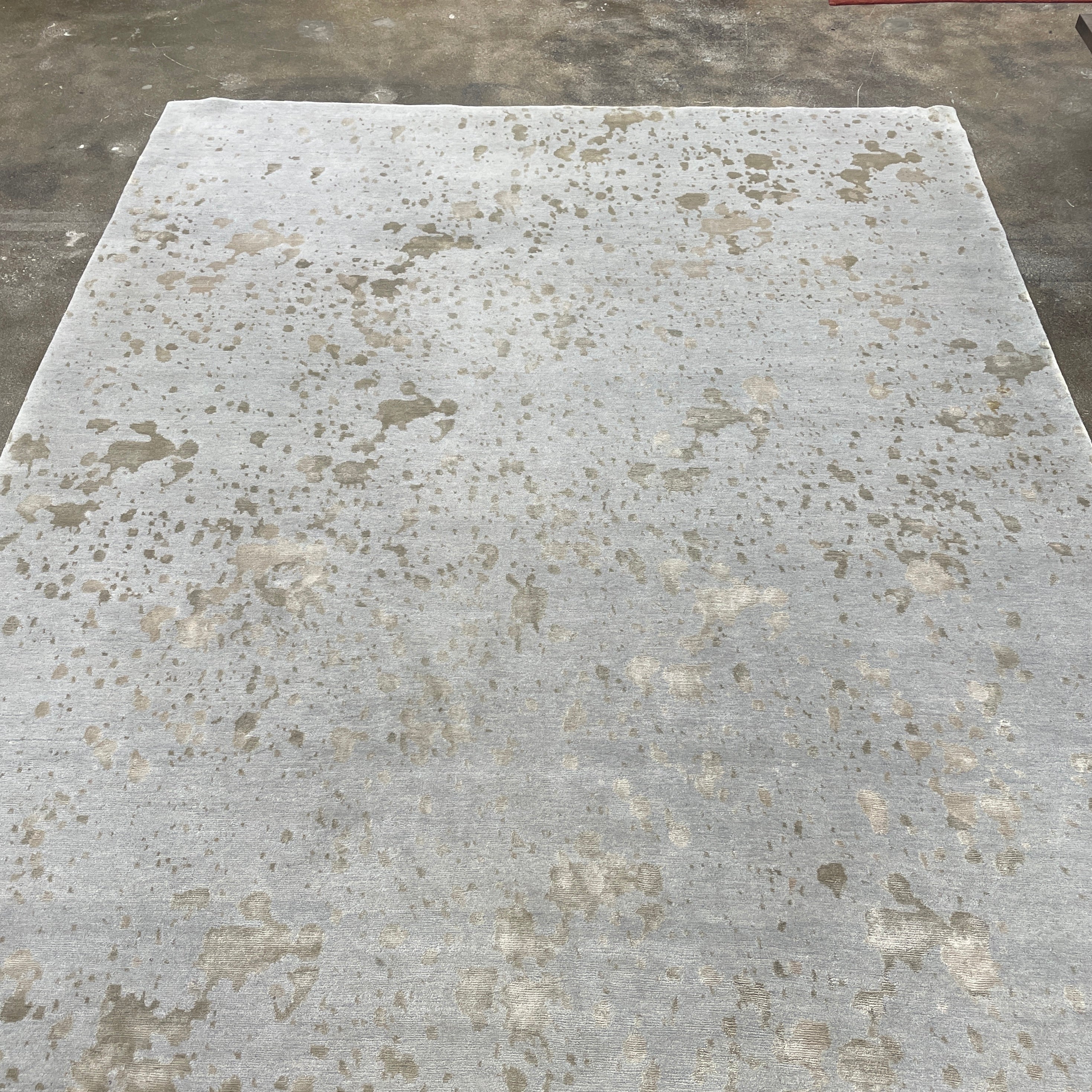 A section of the Delinear's 8 x 10 Delinier Splatter Rug features an abstract design with beige and gray spots, enhanced by Swiss Chromium Dye on Himalayan wool for vibrant detail.