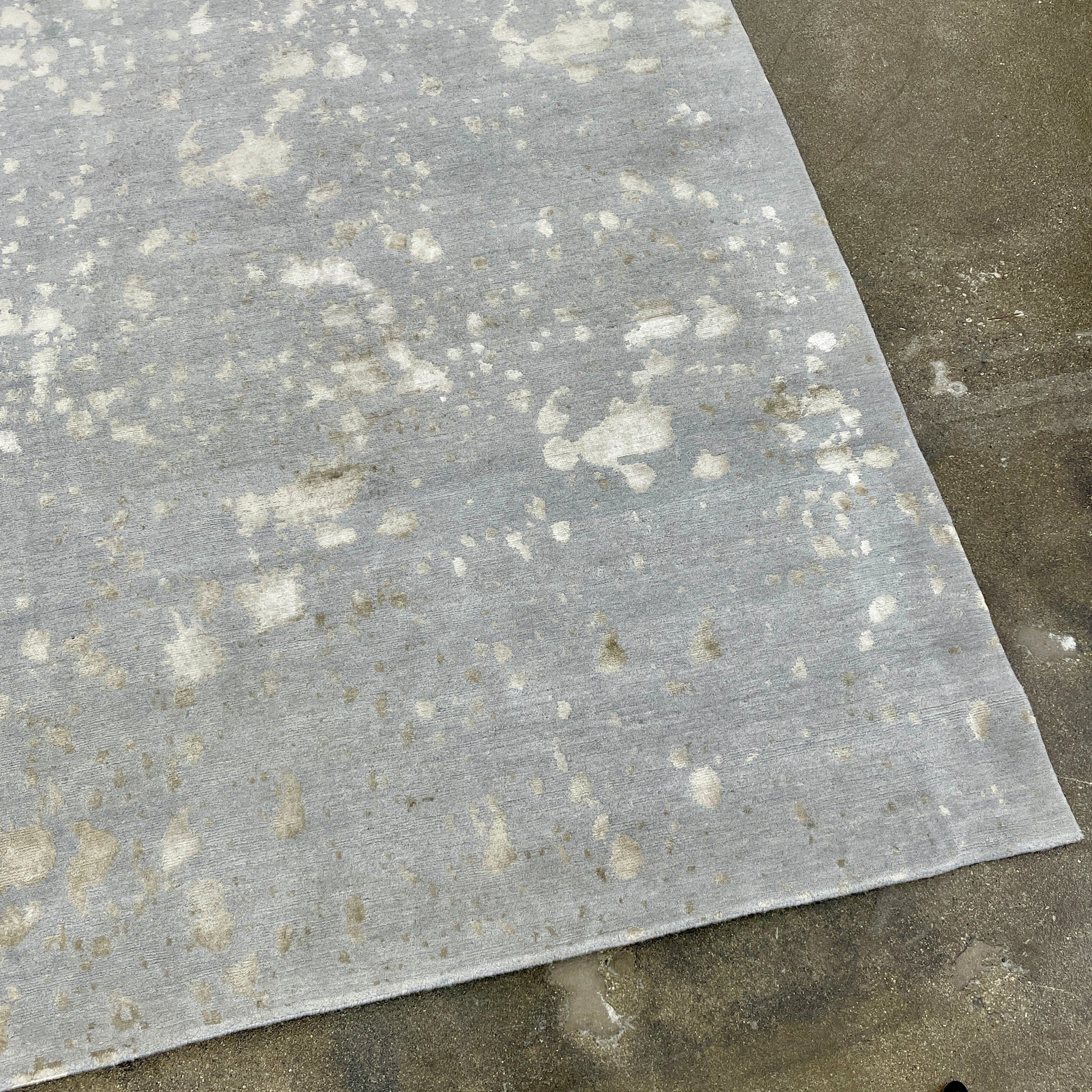 A section of the Delinear's 8 x 10 Delinier Splatter Rug features an abstract design with beige and gray spots, enhanced by Swiss Chromium Dye on Himalayan wool for vibrant detail.