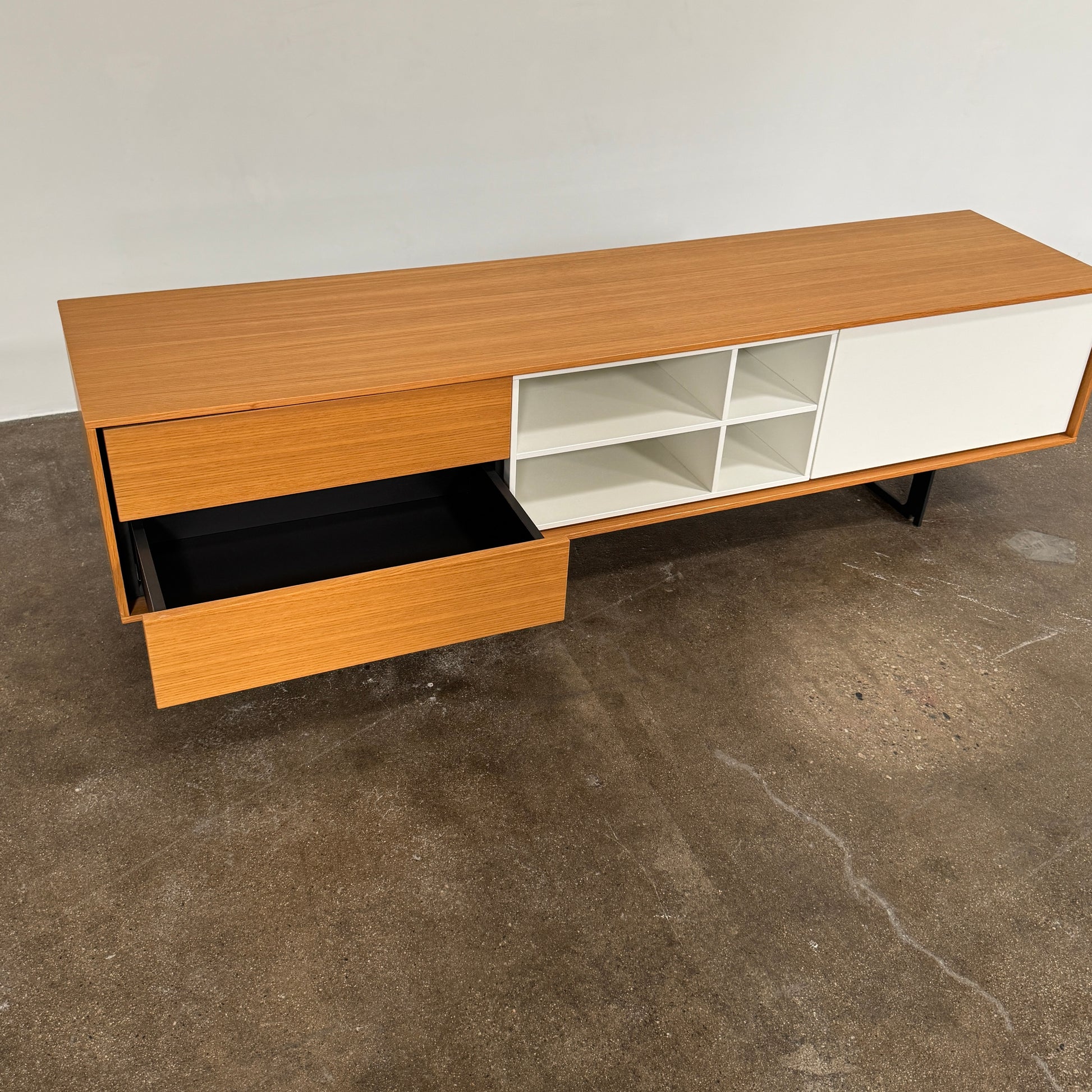 The Treku Aura Media Console by Treku features black metal legs, three left drawers, four open white center shelves, and a right white cabinet door—ideal for minimalist design and organizing your media equipment.