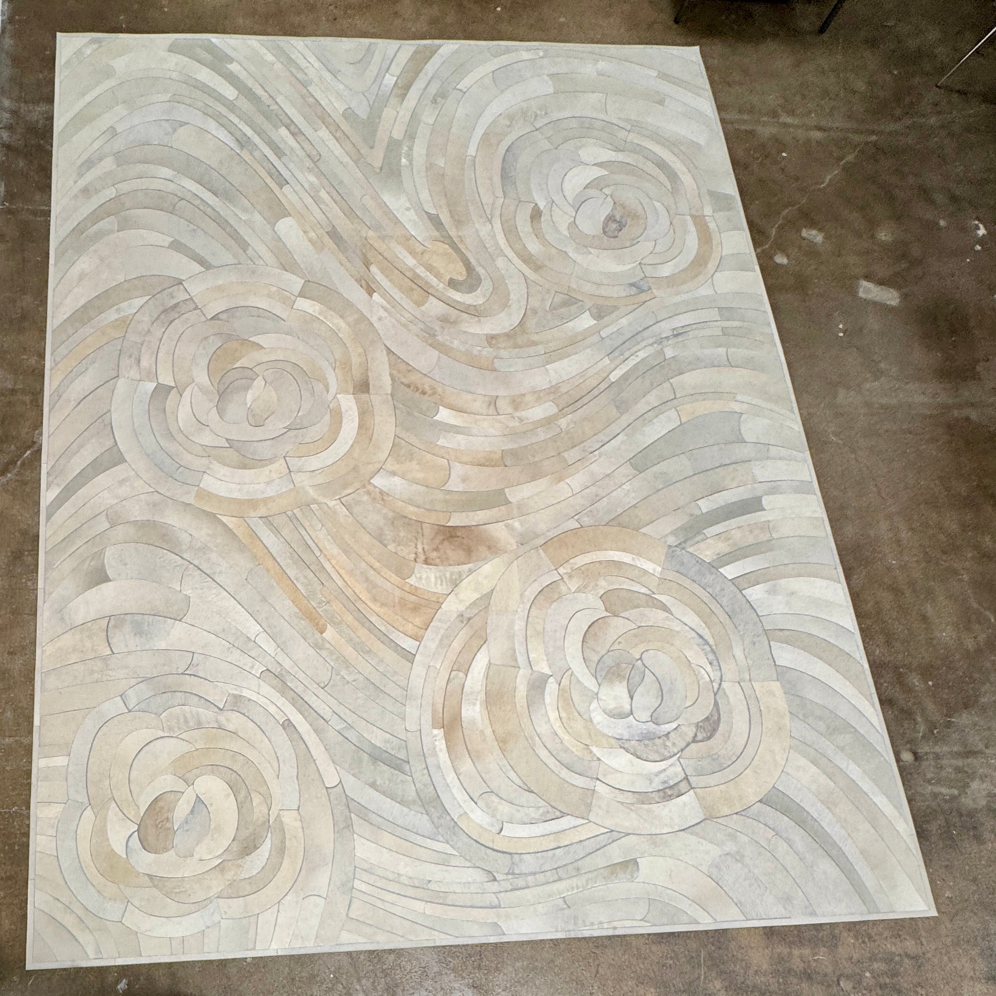 The Kyle Bunting Hide Rug - Drift by Kyle Bunting features a rectangular form with wavy, swirling abstract patterns in beige, cream, and light gray, accented by circular, flower-like designs that highlight exquisite craftsmanship.