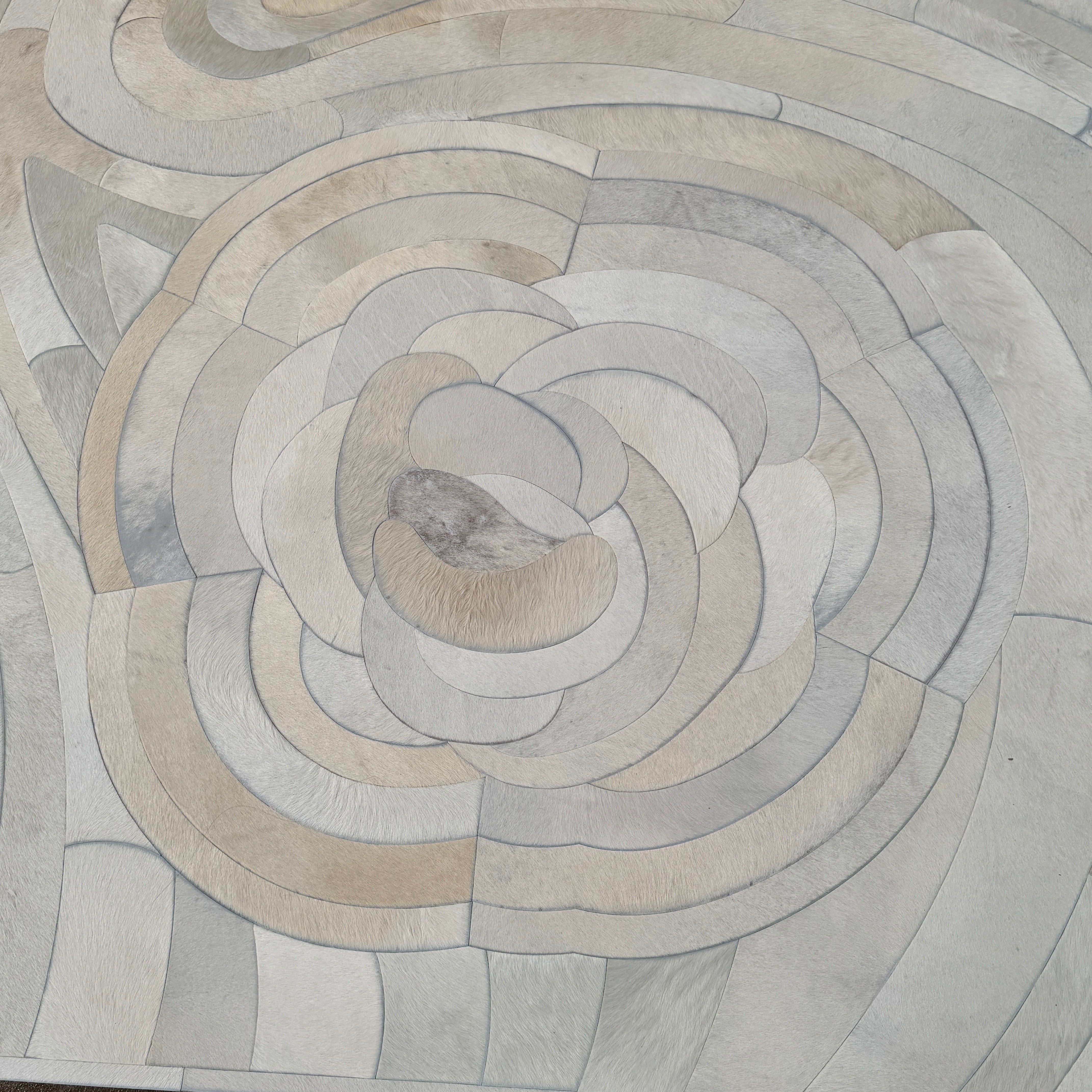 The Kyle Bunting Hide Rug - Drift by Kyle Bunting features a rectangular form with wavy, swirling abstract patterns in beige, cream, and light gray, accented by circular, flower-like designs that highlight exquisite craftsmanship.