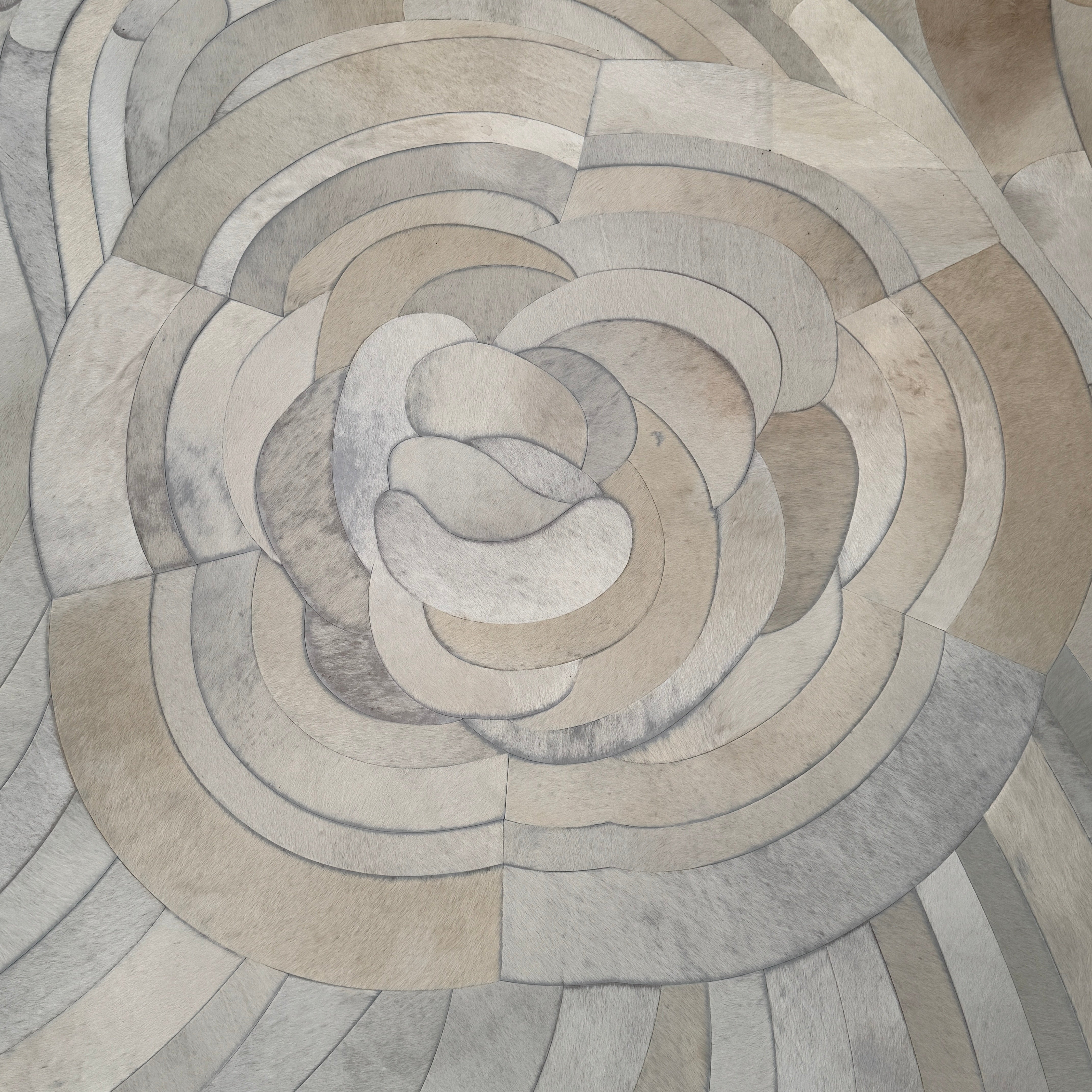 The Kyle Bunting Hide Rug - Drift by Kyle Bunting features a rectangular form with wavy, swirling abstract patterns in beige, cream, and light gray, accented by circular, flower-like designs that highlight exquisite craftsmanship.