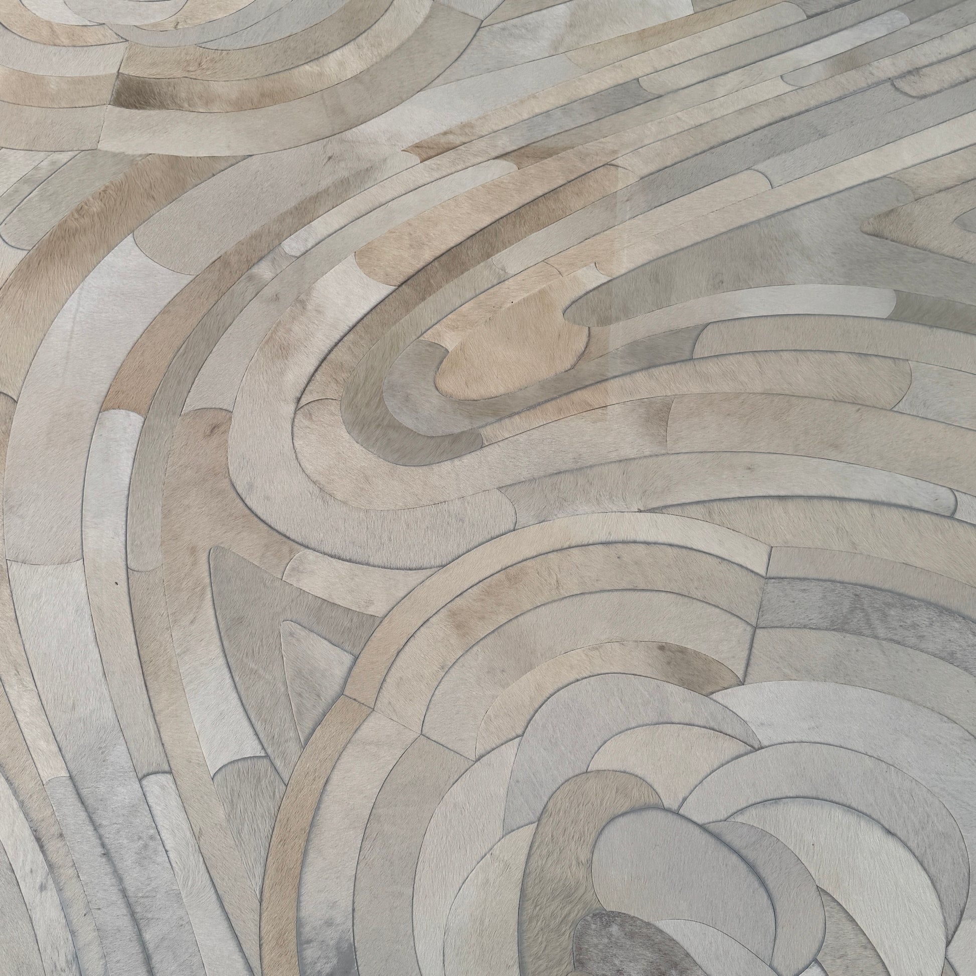 The Kyle Bunting Hide Rug - Drift by Kyle Bunting features a rectangular form with wavy, swirling abstract patterns in beige, cream, and light gray, accented by circular, flower-like designs that highlight exquisite craftsmanship.