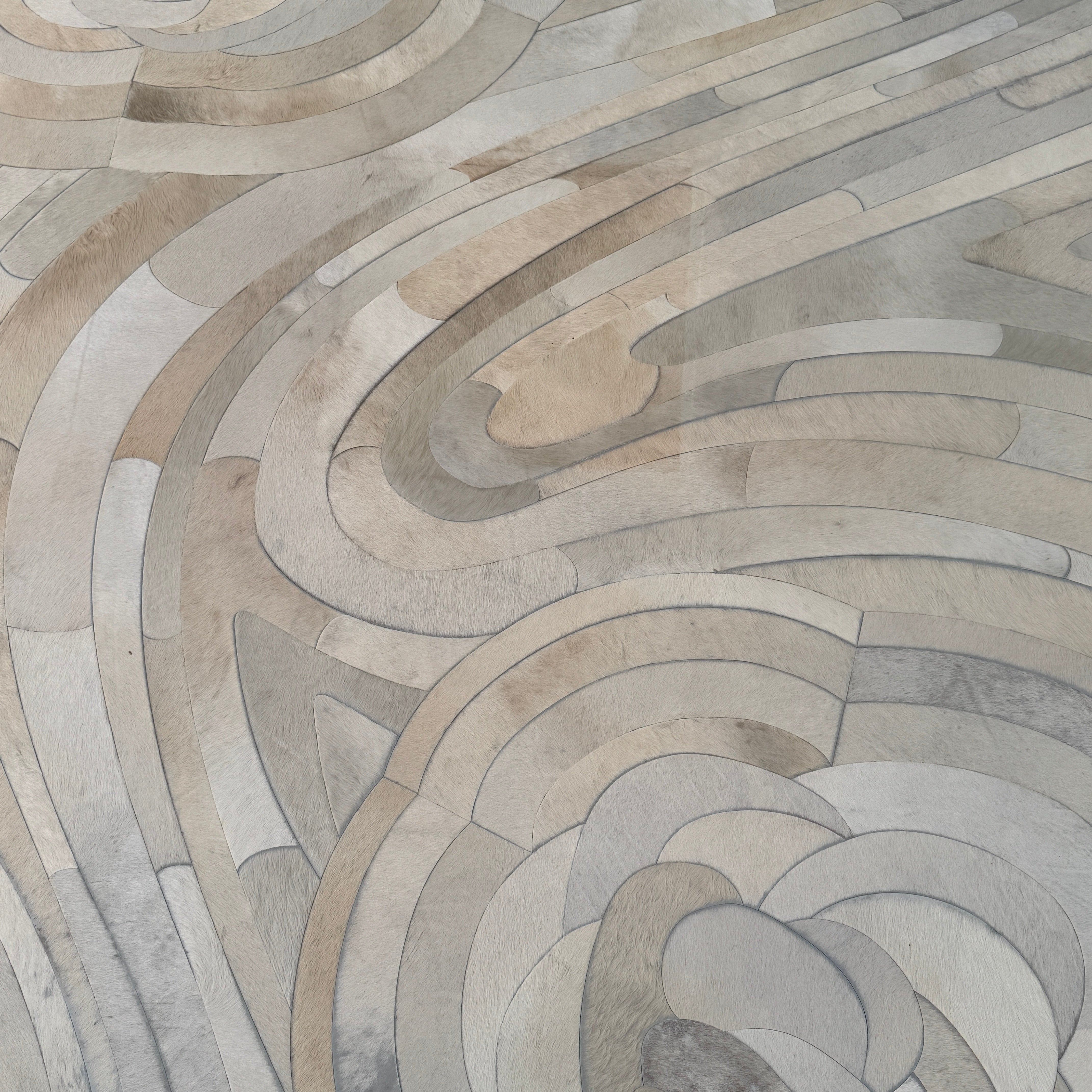 The Kyle Bunting Hide Rug - Drift by Kyle Bunting features a rectangular form with wavy, swirling abstract patterns in beige, cream, and light gray, accented by circular, flower-like designs that highlight exquisite craftsmanship.