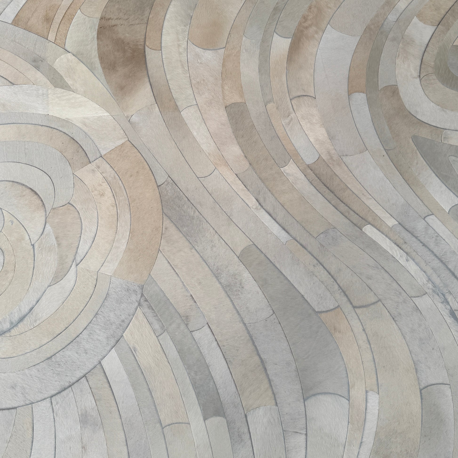 The Kyle Bunting Hide Rug - Drift by Kyle Bunting features a rectangular form with wavy, swirling abstract patterns in beige, cream, and light gray, accented by circular, flower-like designs that highlight exquisite craftsmanship.