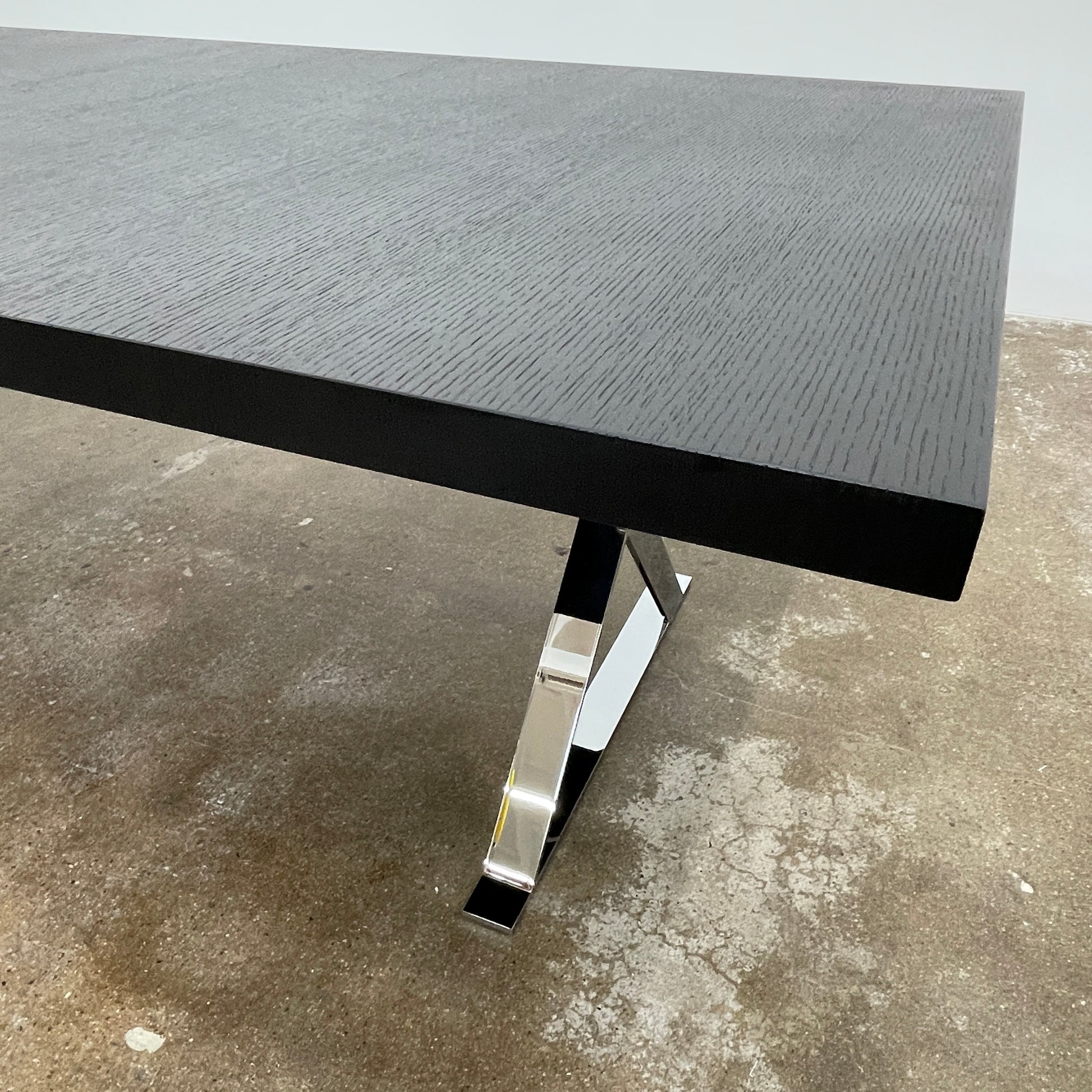The Maxalto Max Dining Table by Maxalto is a minimalist black rectangular table made from brushed black oak, featuring a flat top with modern X-shaped metal legs.