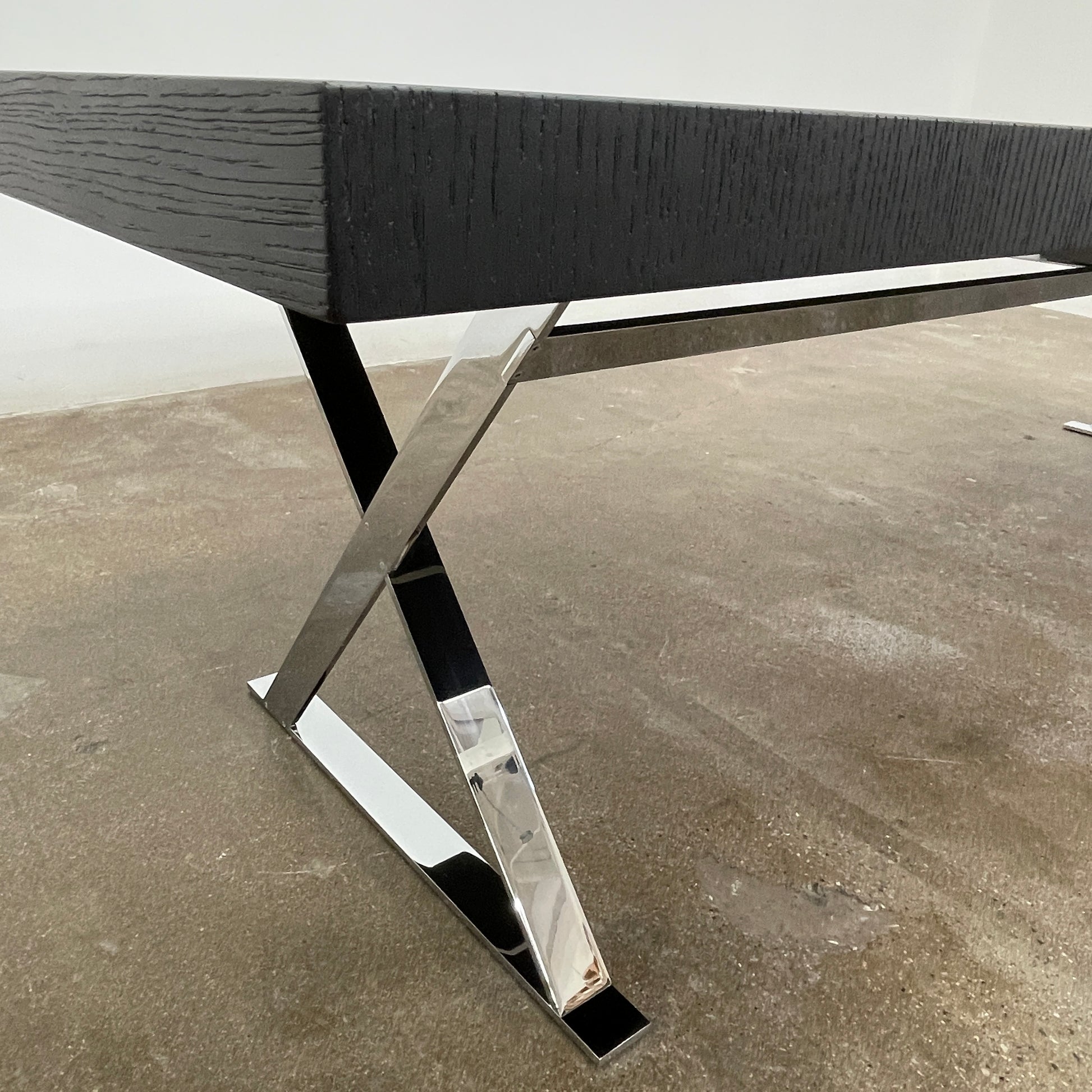 The Maxalto Max Dining Table by Maxalto is a minimalist black rectangular table made from brushed black oak, featuring a flat top with modern X-shaped metal legs.