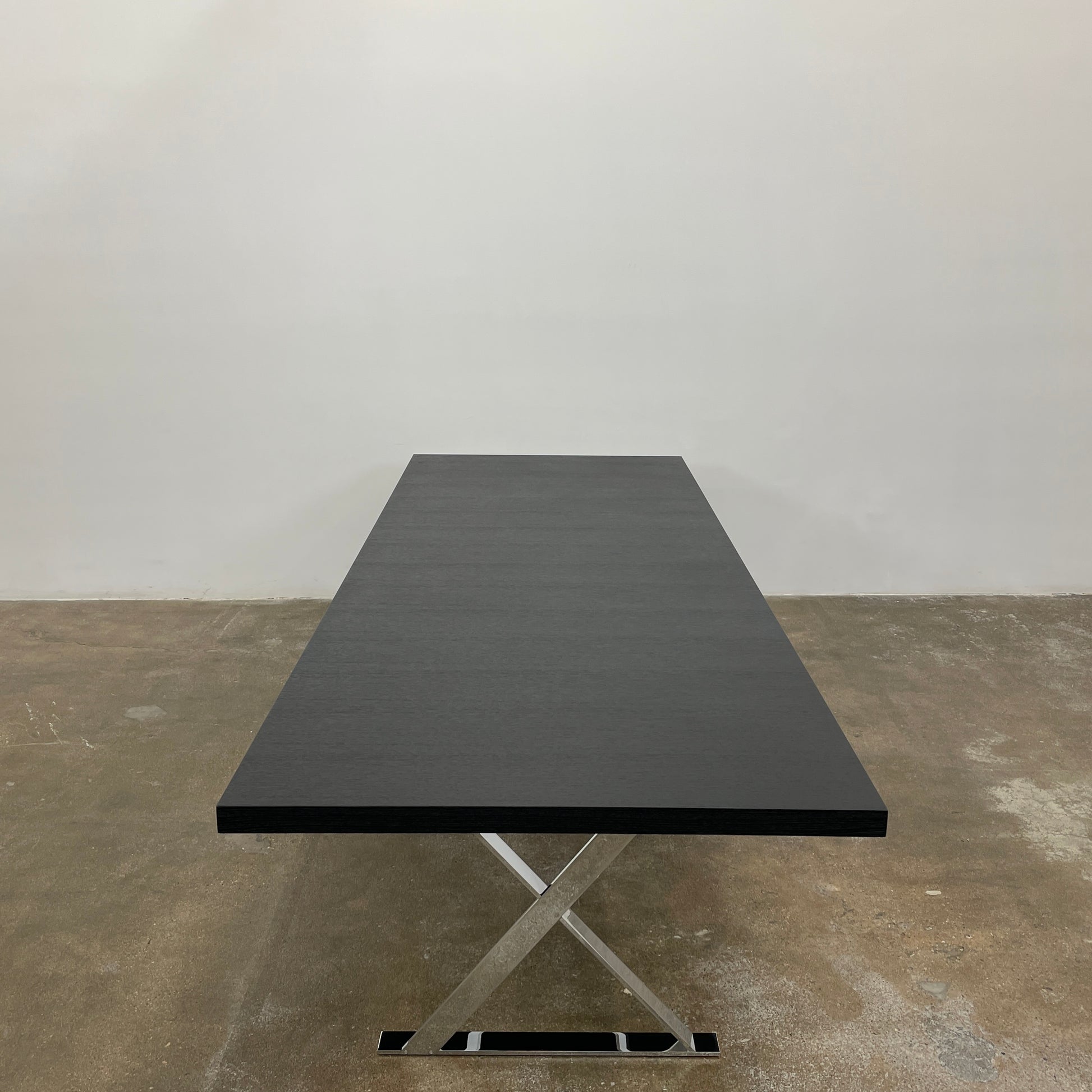 The Maxalto Max Dining Table by Maxalto is a minimalist black rectangular table made from brushed black oak, featuring a flat top with modern X-shaped metal legs.