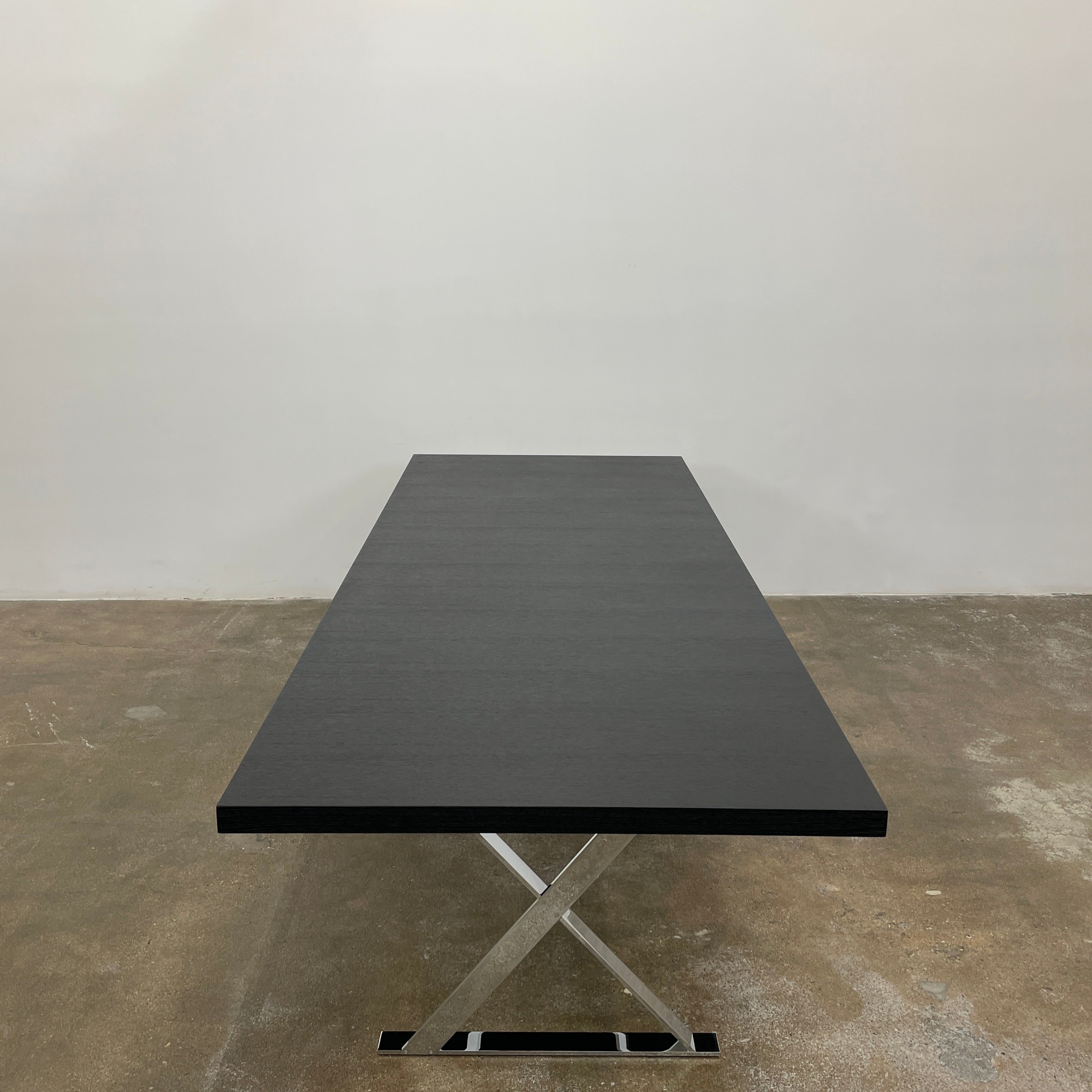 The Maxalto Max Dining Table by Maxalto is a minimalist black rectangular table made from brushed black oak, featuring a flat top with modern X-shaped metal legs.