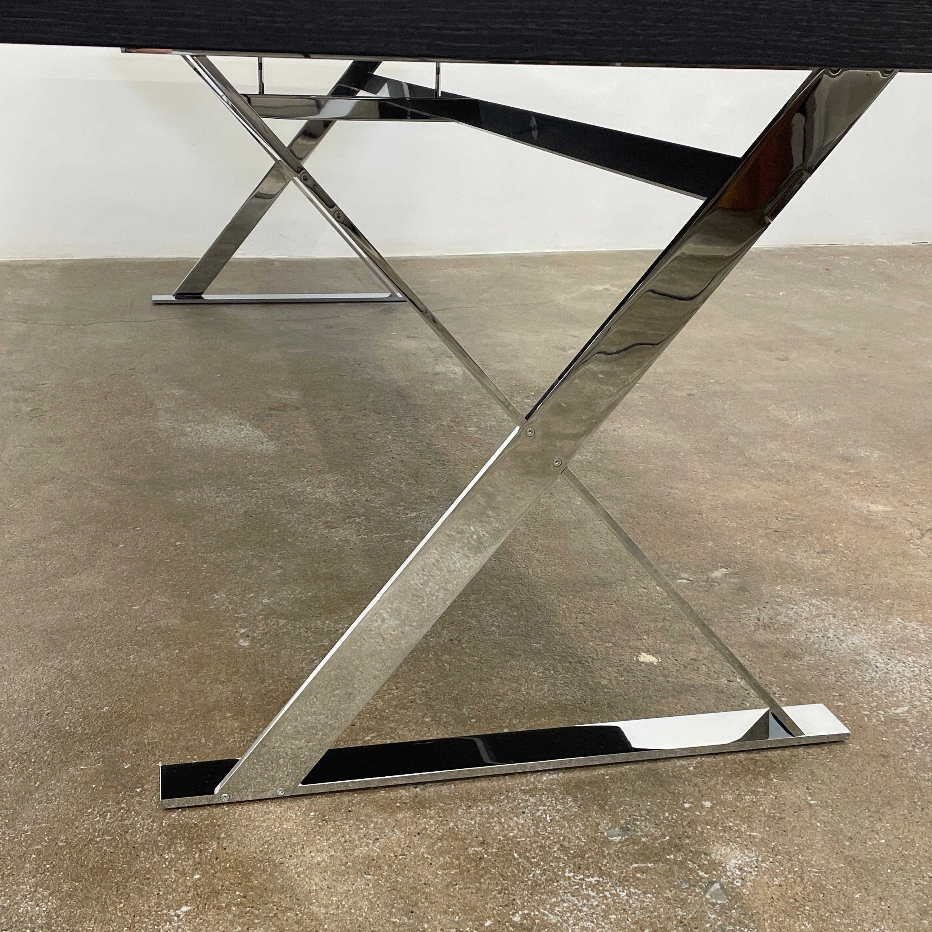 The Maxalto Max Dining Table by Maxalto is a minimalist black rectangular table made from brushed black oak, featuring a flat top with modern X-shaped metal legs.