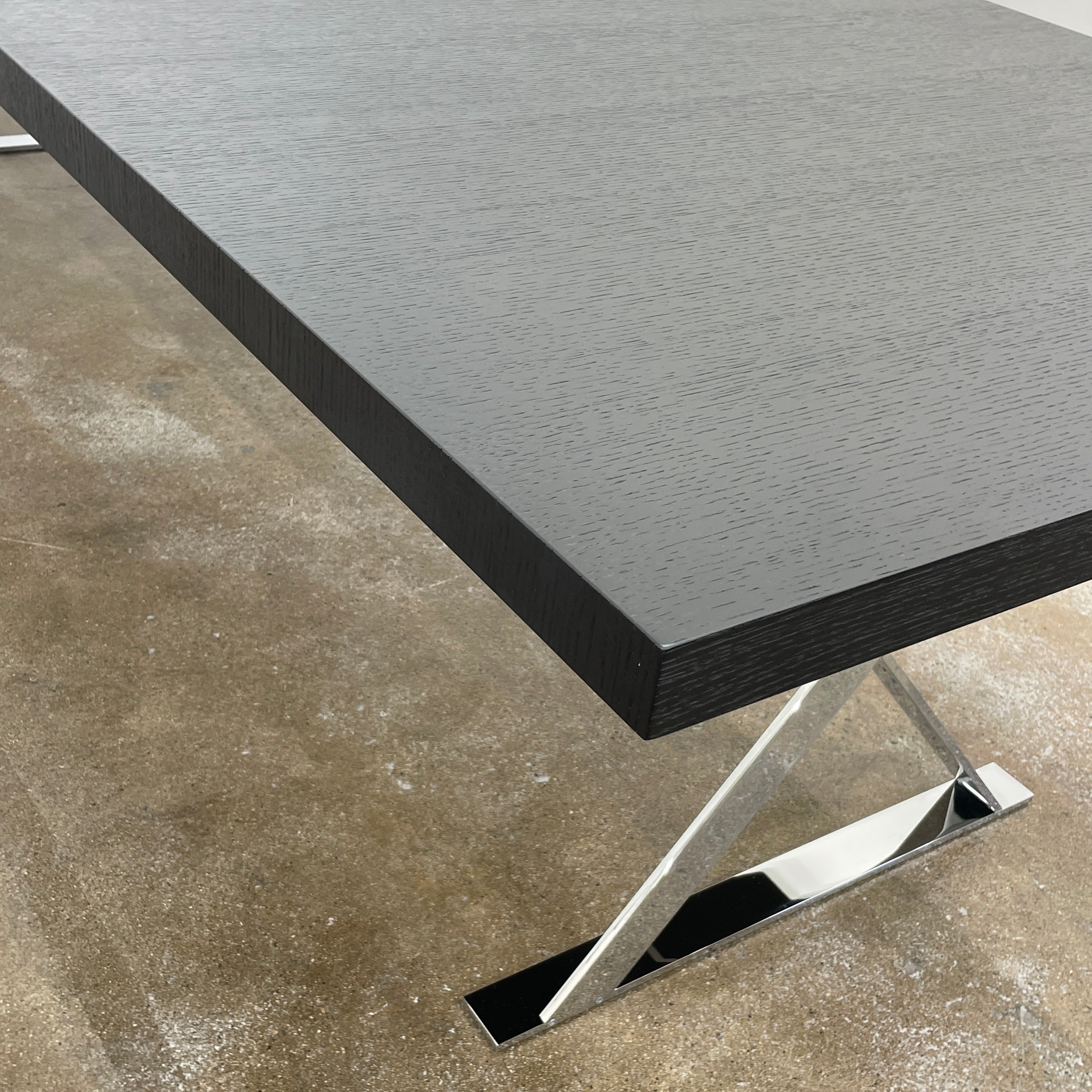 The Maxalto Max Dining Table by Maxalto is a minimalist black rectangular table made from brushed black oak, featuring a flat top with modern X-shaped metal legs.