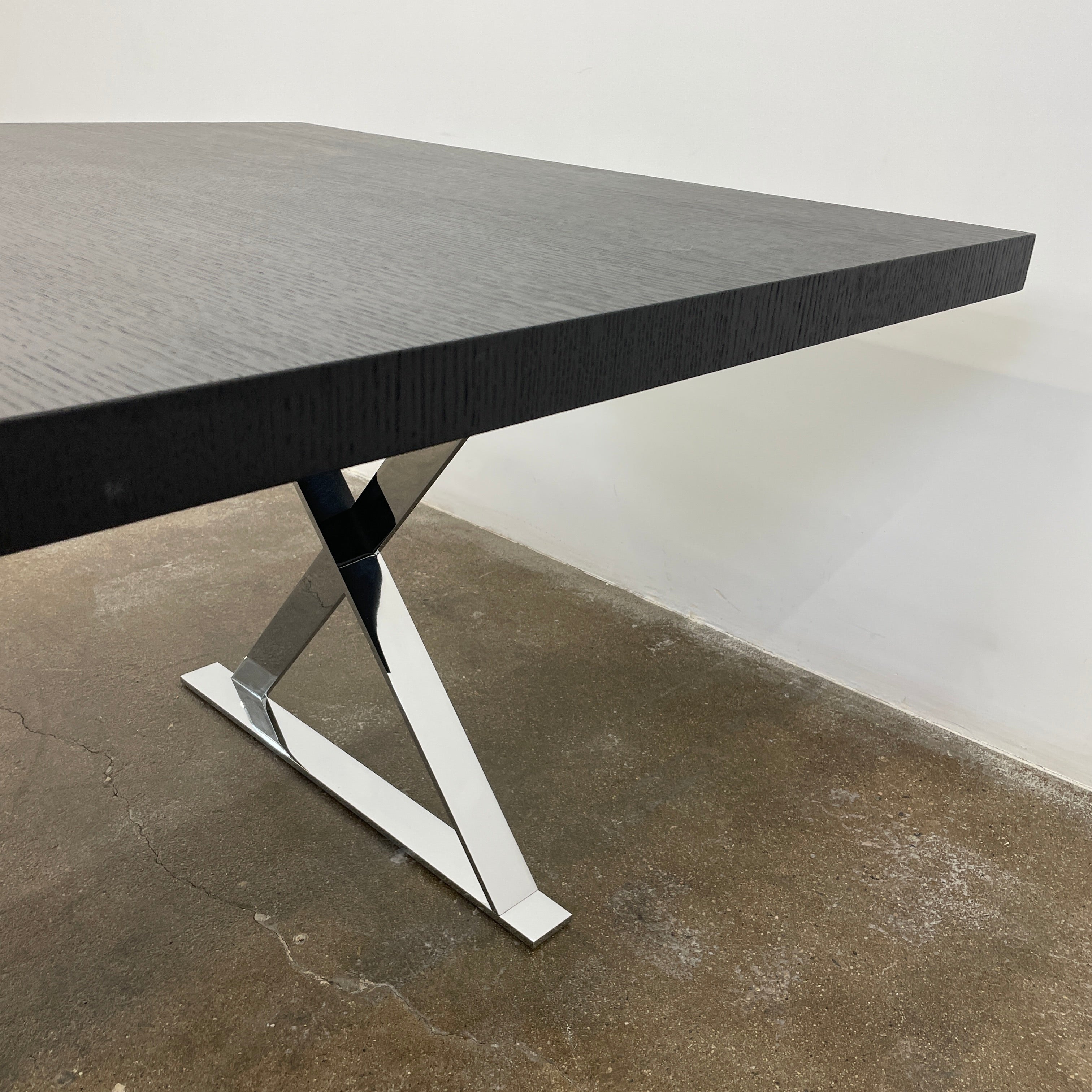 The Maxalto Max Dining Table by Maxalto is a minimalist black rectangular table made from brushed black oak, featuring a flat top with modern X-shaped metal legs.