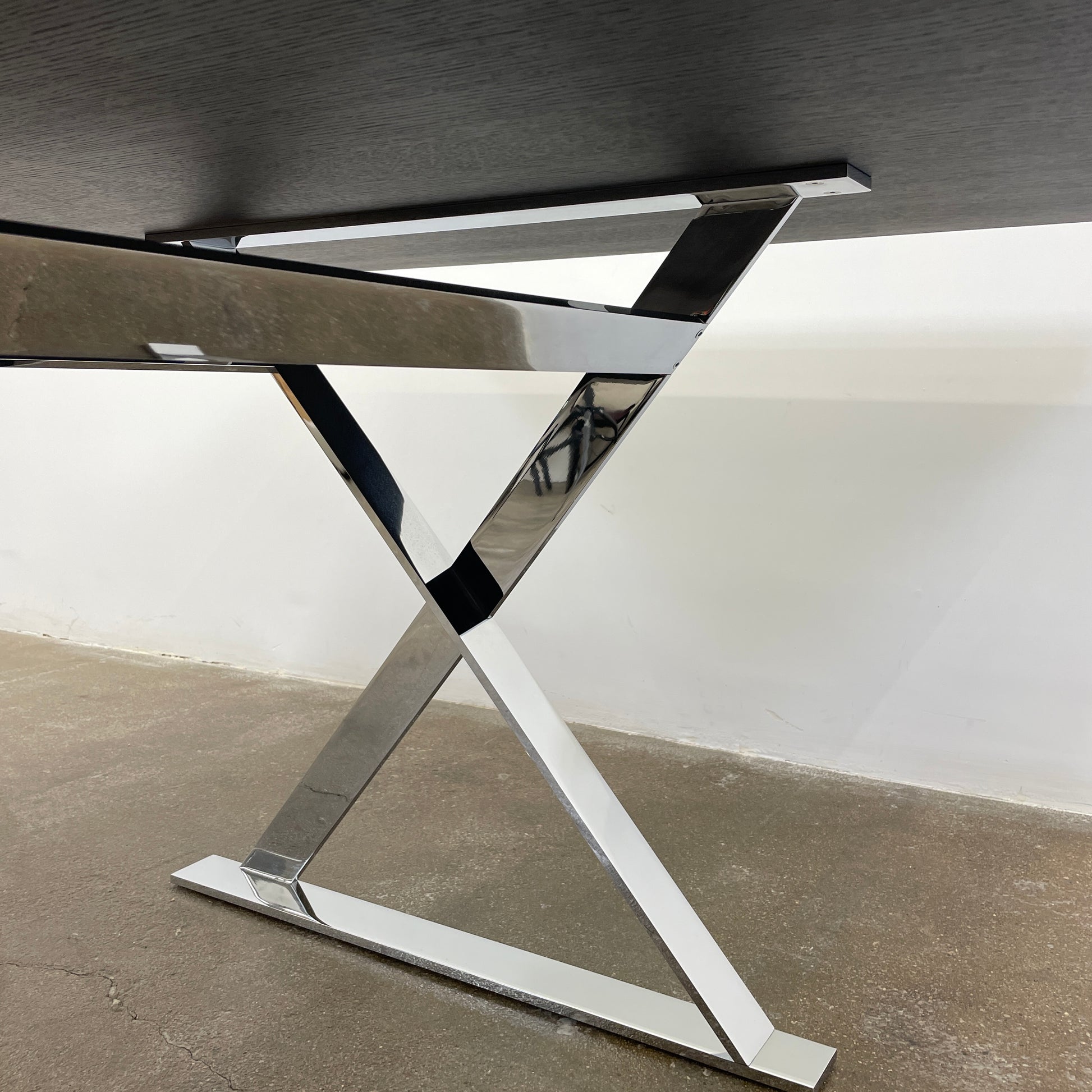 The Maxalto Max Dining Table by Maxalto is a minimalist black rectangular table made from brushed black oak, featuring a flat top with modern X-shaped metal legs.