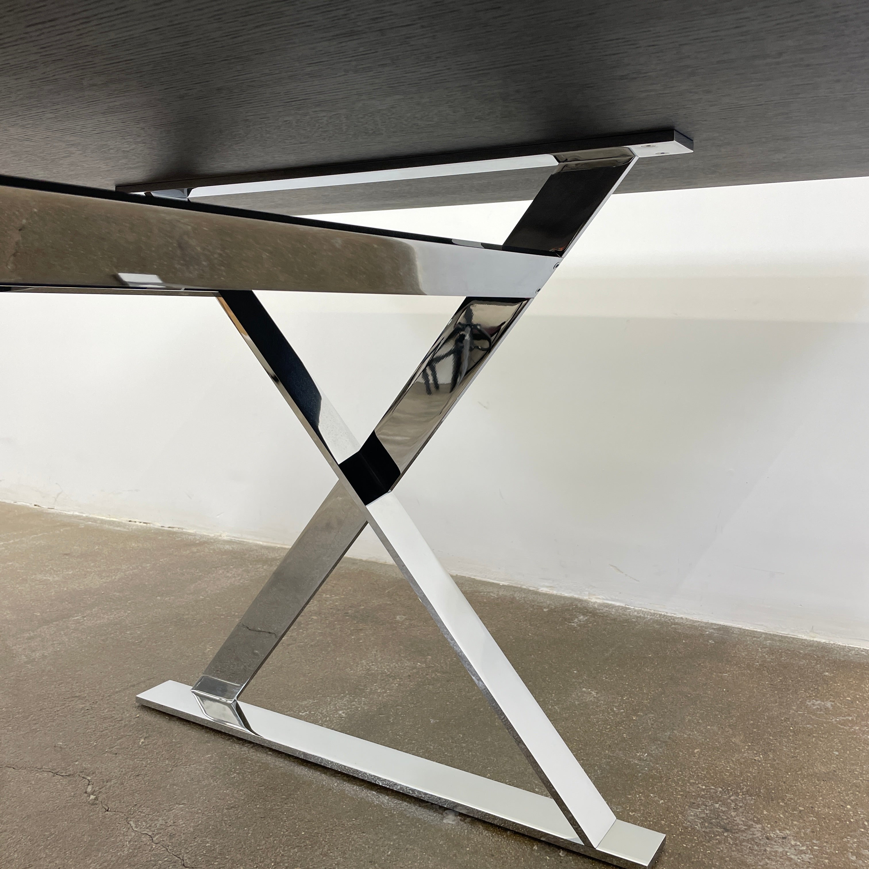 The Maxalto Max Dining Table by Maxalto is a minimalist black rectangular table made from brushed black oak, featuring a flat top with modern X-shaped metal legs.