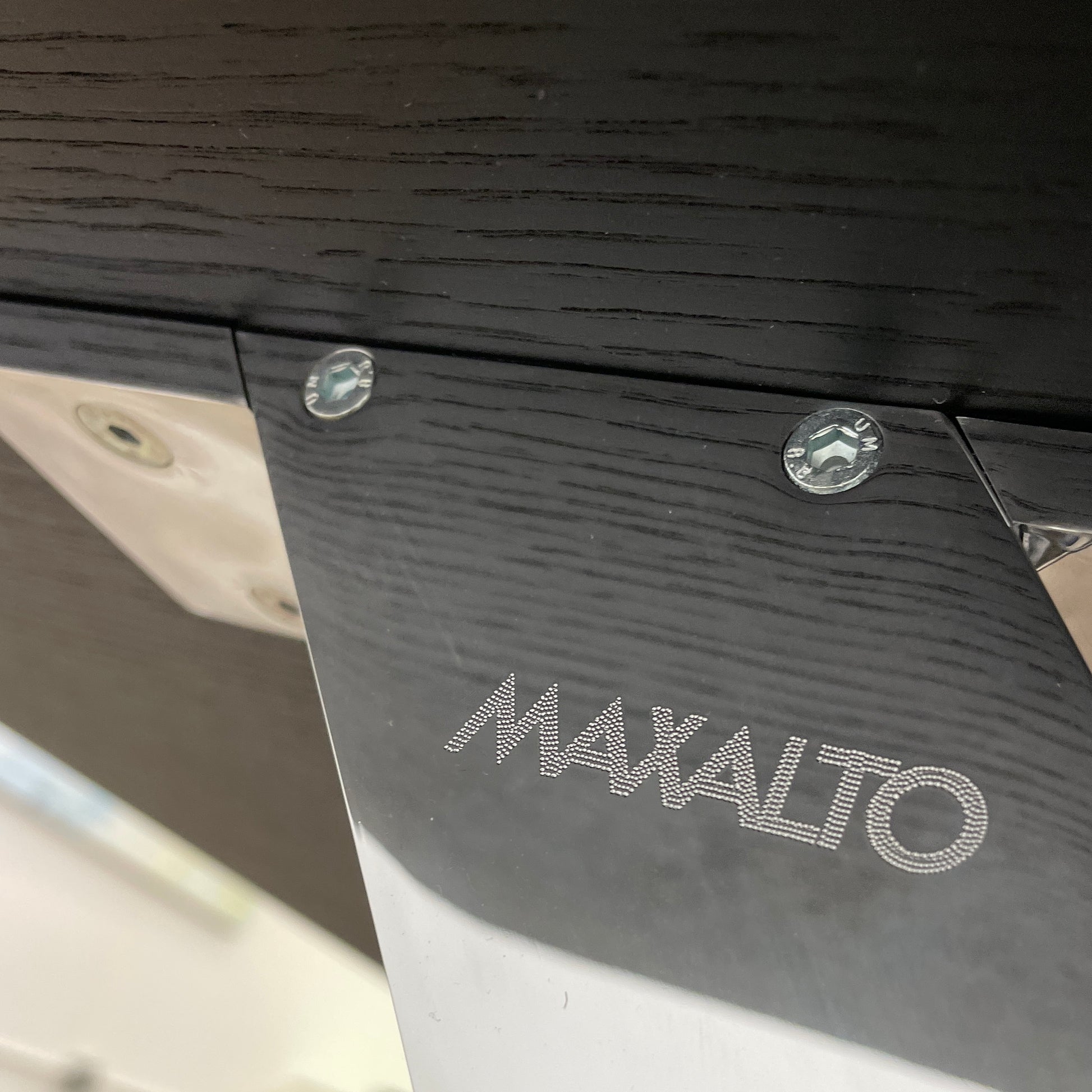 The Maxalto Max Dining Table by Maxalto is a minimalist black rectangular table made from brushed black oak, featuring a flat top with modern X-shaped metal legs.