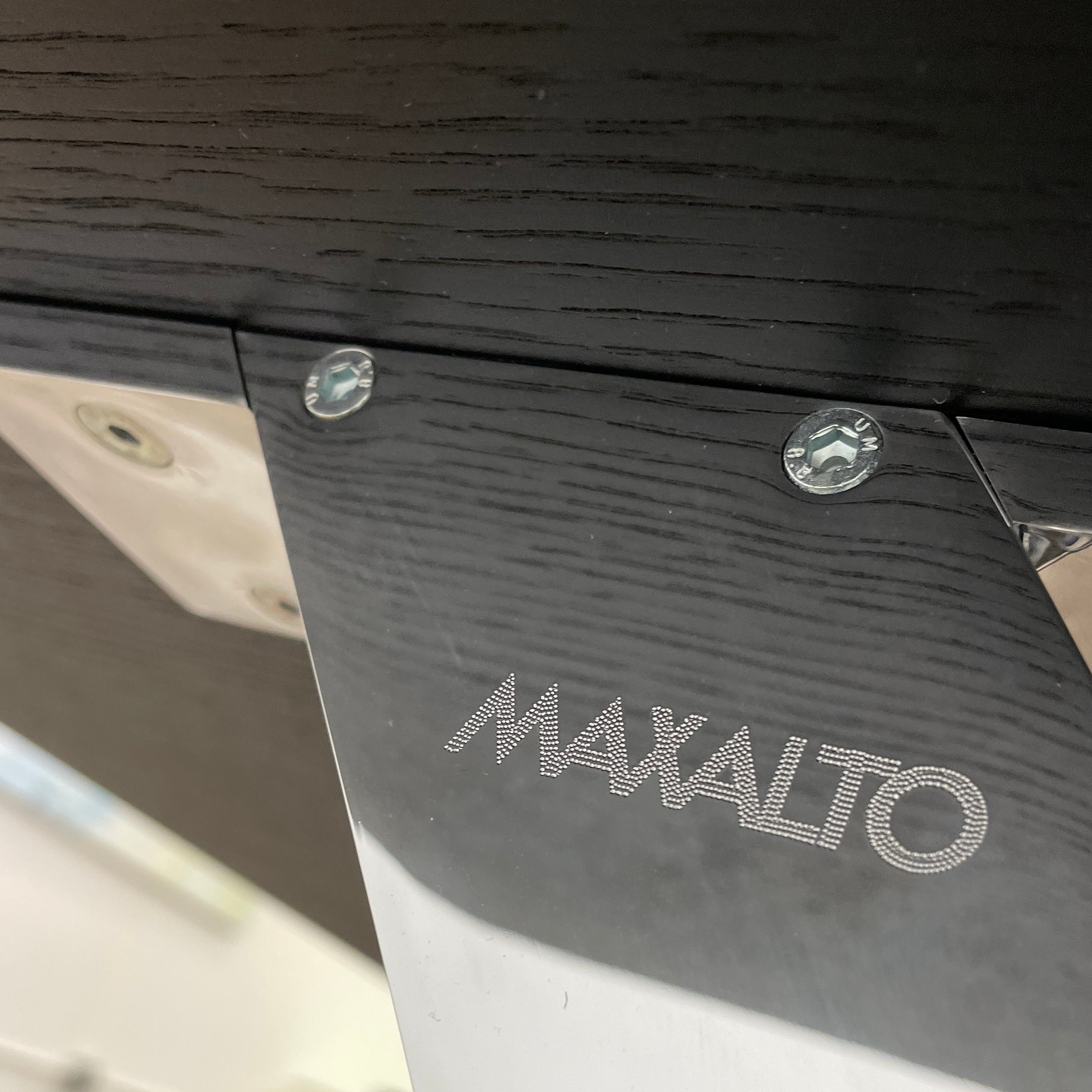 The Maxalto Max Dining Table by Maxalto is a minimalist black rectangular table made from brushed black oak, featuring a flat top with modern X-shaped metal legs.