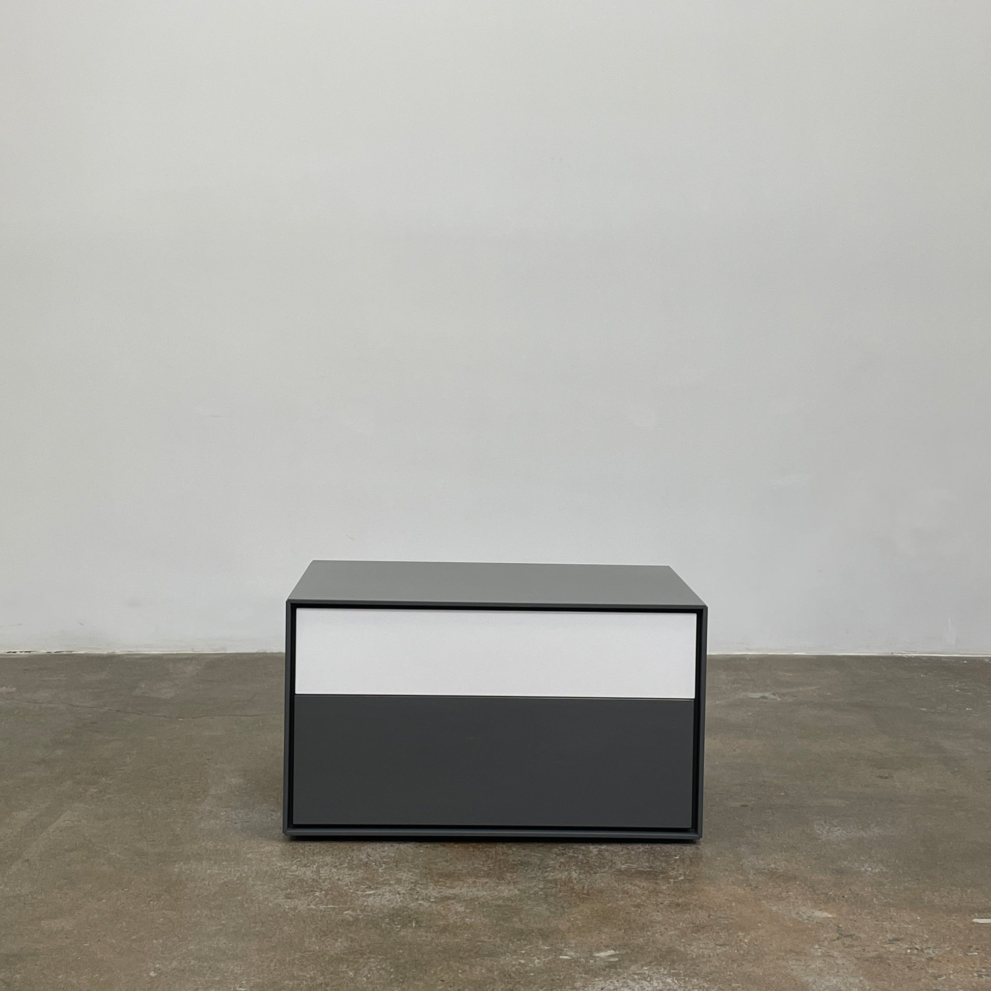 A rectangular gray and white lacquer box from B&B Italia, reminiscent of the Dado Night Table's minimalist design, features a glossy upper and matte lower section. This sleek piece serves as a stylish bedside companion, enhancing any modern space against a plain white background.