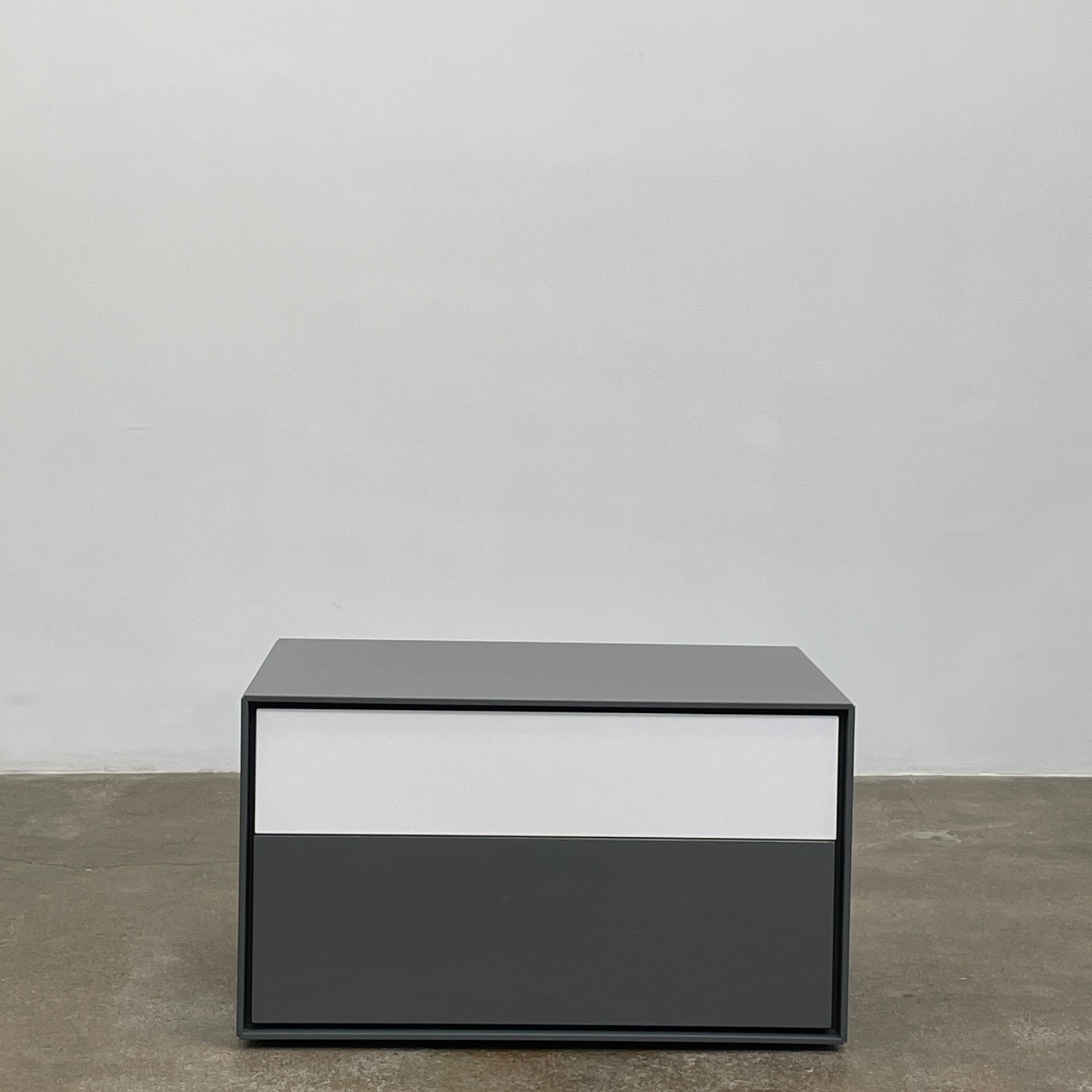 A rectangular gray and white lacquer box from B&B Italia, reminiscent of the Dado Night Table's minimalist design, features a glossy upper and matte lower section. This sleek piece serves as a stylish bedside companion, enhancing any modern space against a plain white background.