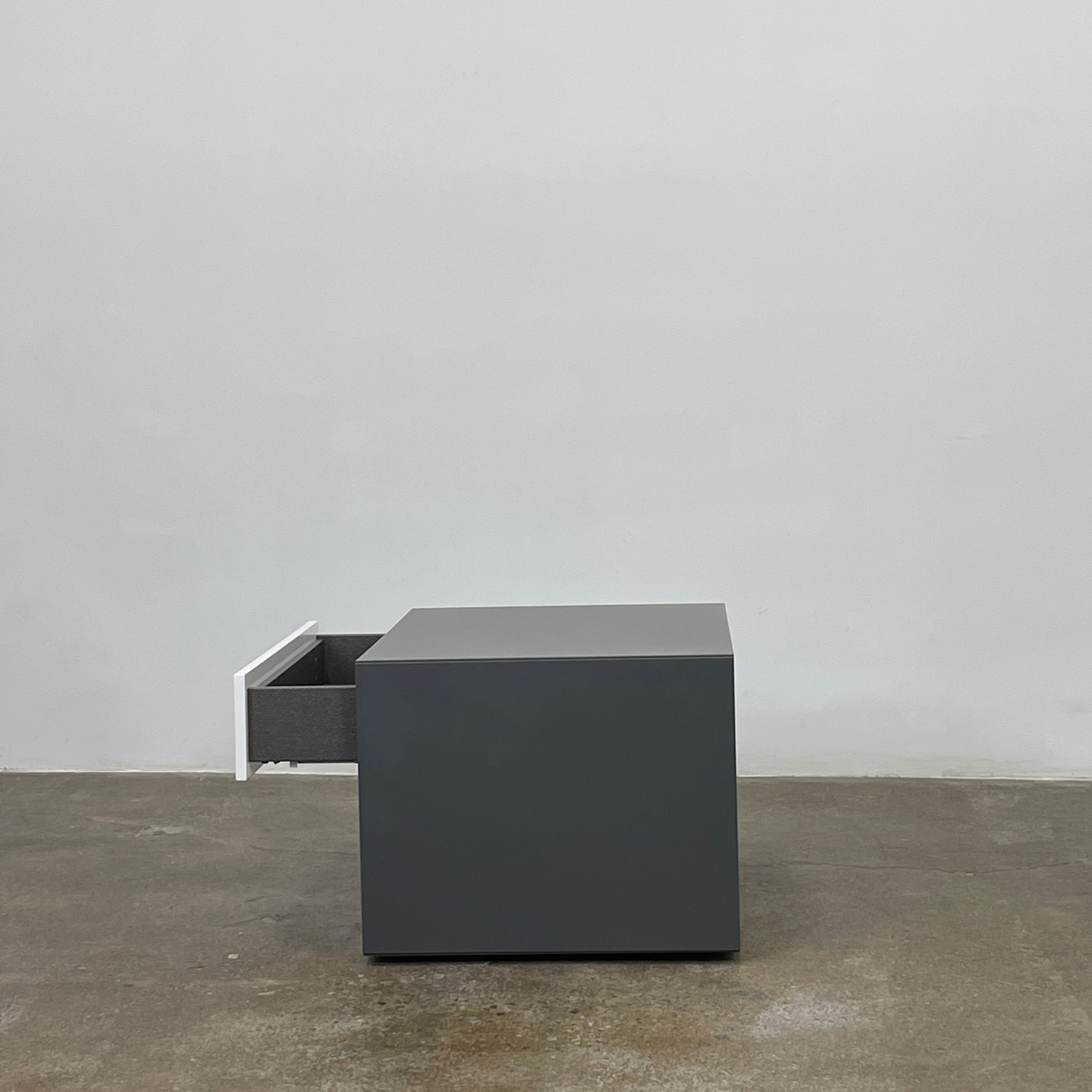 A rectangular gray and white lacquer box from B&B Italia, reminiscent of the Dado Night Table's minimalist design, features a glossy upper and matte lower section. This sleek piece serves as a stylish bedside companion, enhancing any modern space against a plain white background.