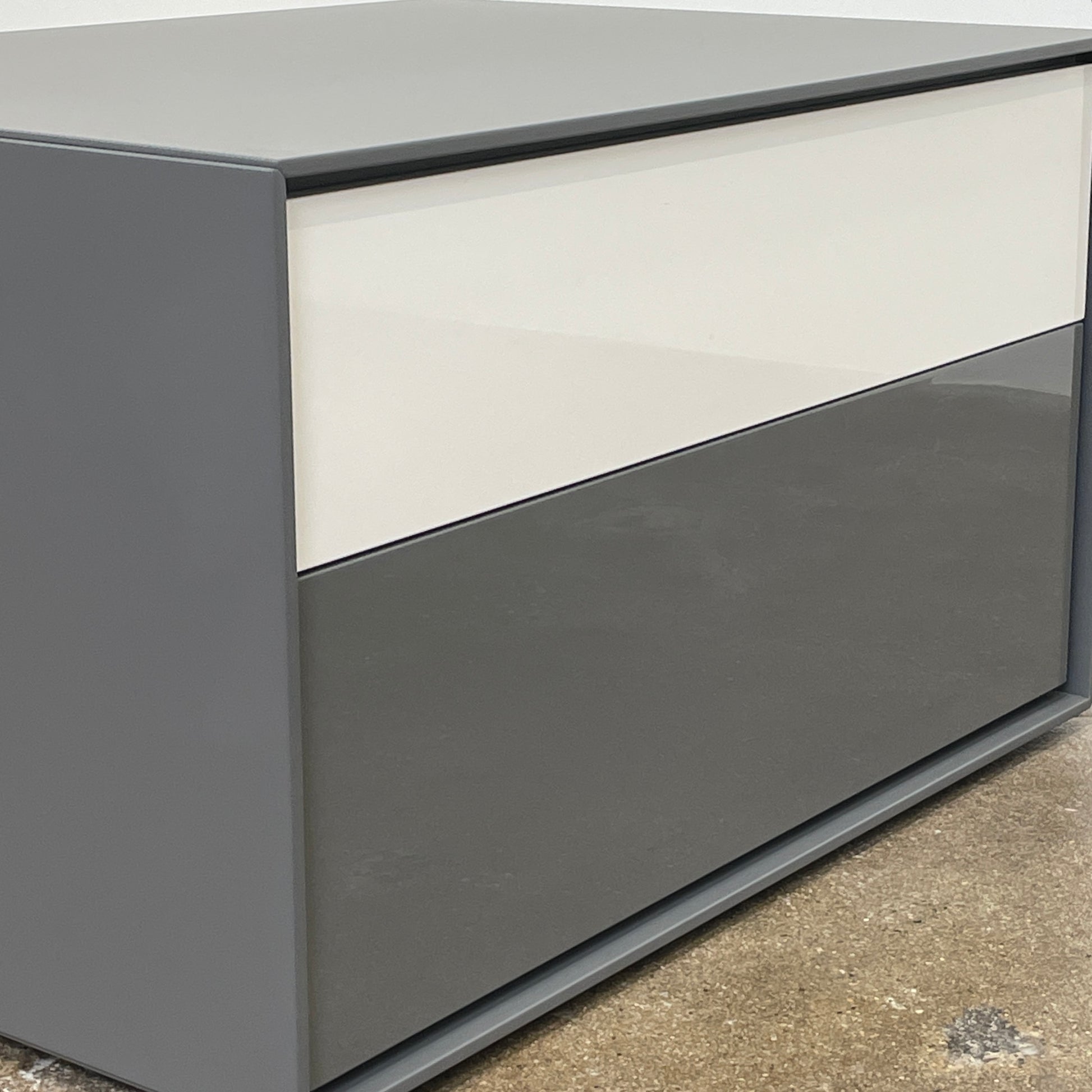 A rectangular gray and white lacquer box from B&B Italia, reminiscent of the Dado Night Table's minimalist design, features a glossy upper and matte lower section. This sleek piece serves as a stylish bedside companion, enhancing any modern space against a plain white background.