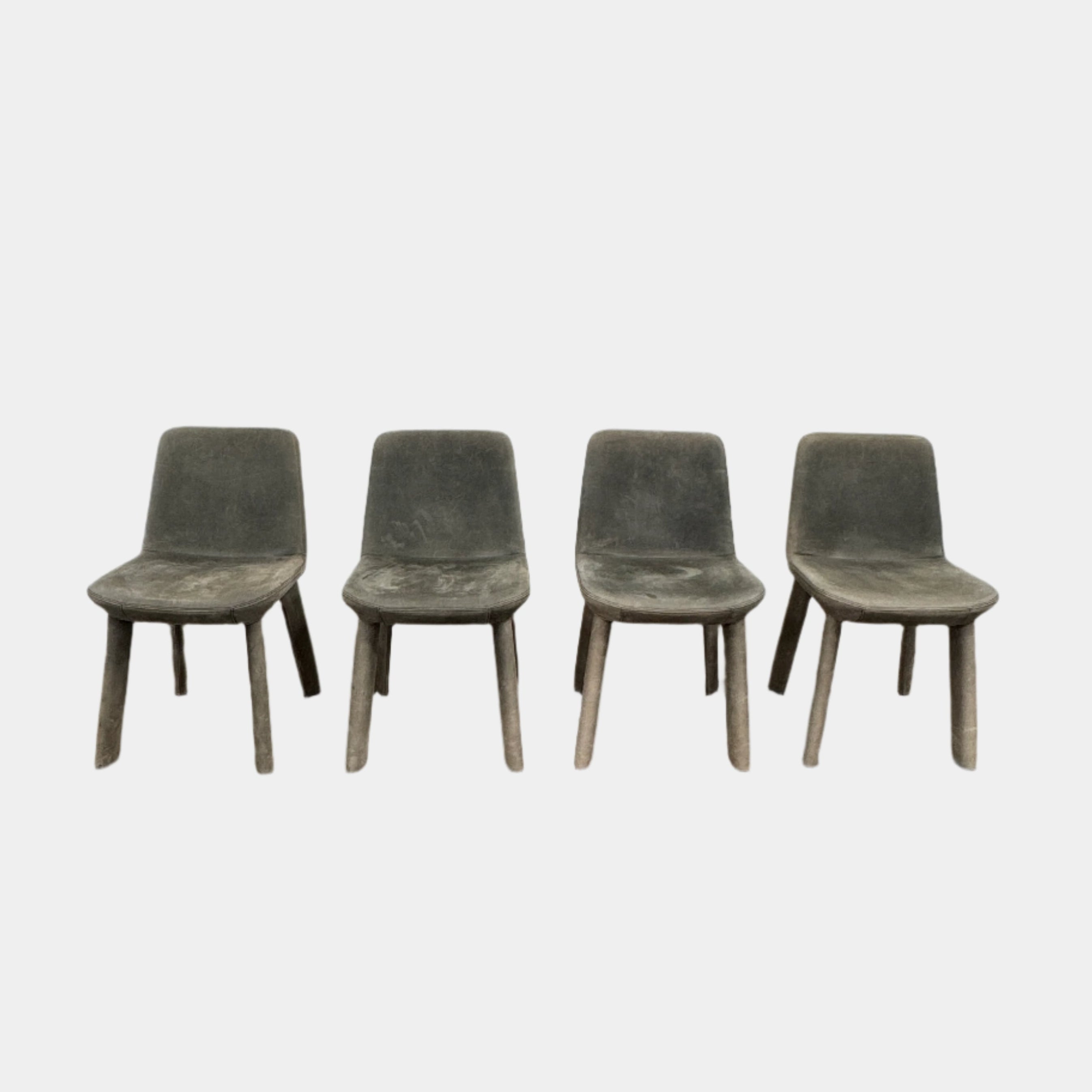 Four Blu Dot Neat Dining Chairs (set of 4, gray) from Blu Dot are lined up against a white wall on a brown concrete floor, highlighting a minimalist and tidy atmosphere.
