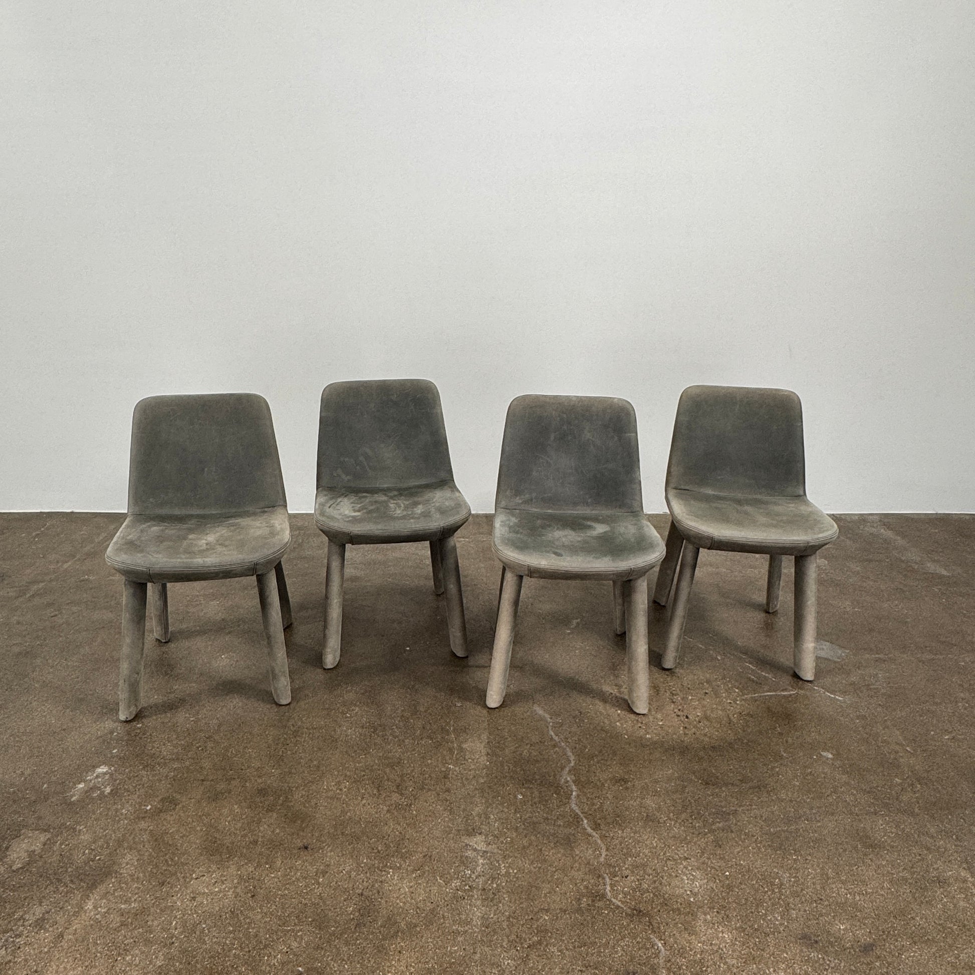 Four Blu Dot Neat Dining Chairs (set of 4, gray) from Blu Dot are lined up against a white wall on a brown concrete floor, highlighting a minimalist and tidy atmosphere.