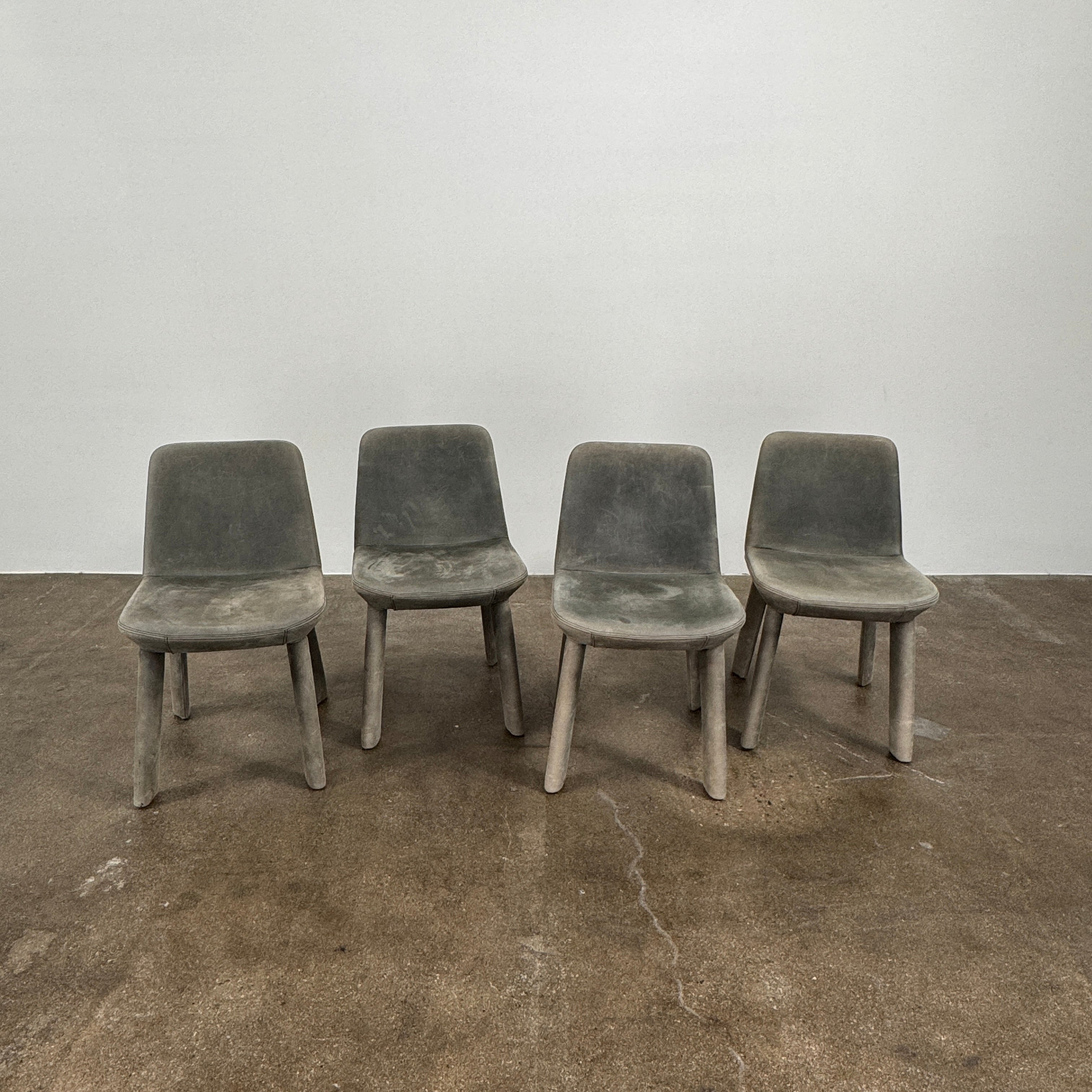 Four Blu Dot Neat Dining Chairs (set of 4, gray) from Blu Dot are lined up against a white wall on a brown concrete floor, highlighting a minimalist and tidy atmosphere.