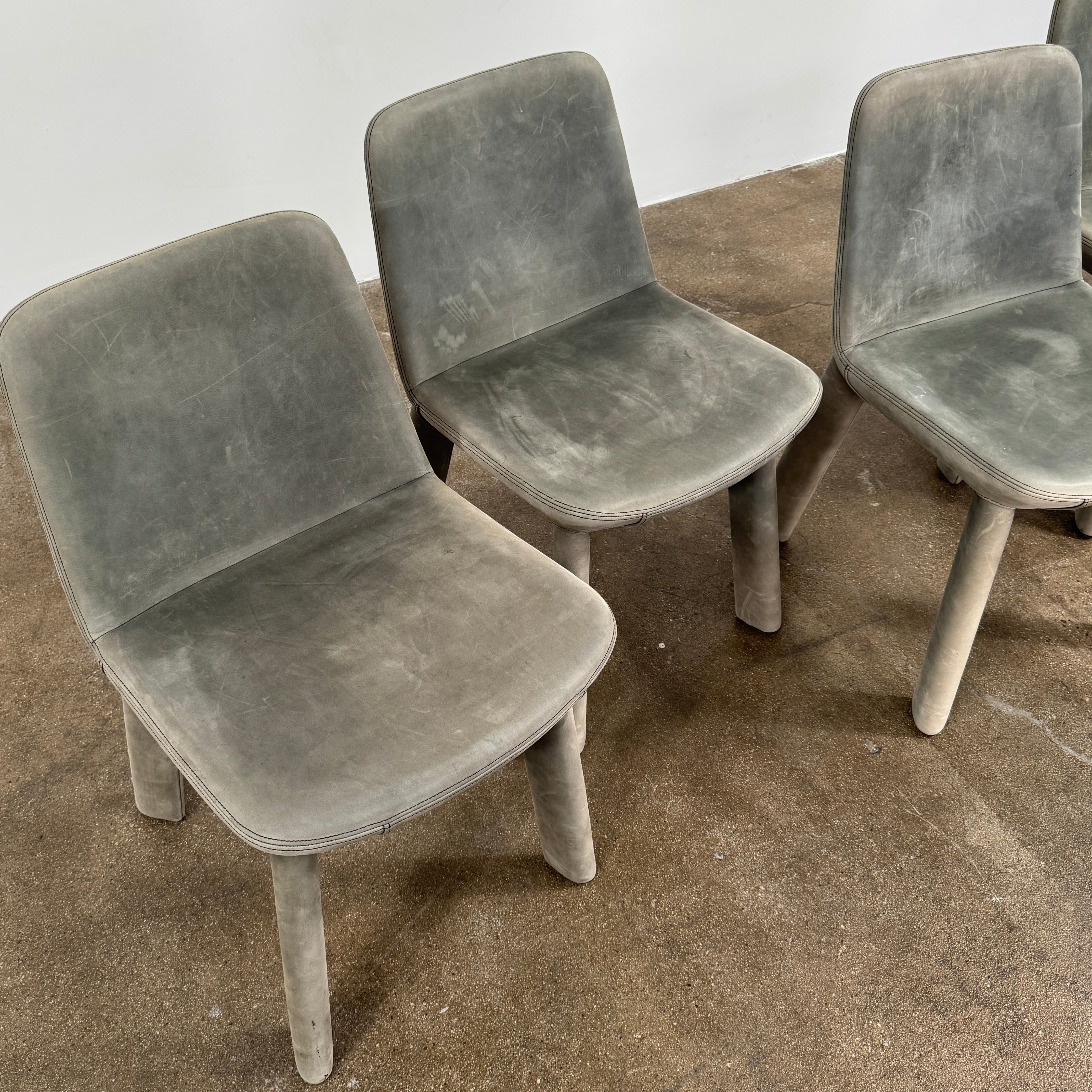 Four Blu Dot Neat Dining Chairs (set of 4, gray) from Blu Dot are lined up against a white wall on a brown concrete floor, highlighting a minimalist and tidy atmosphere.