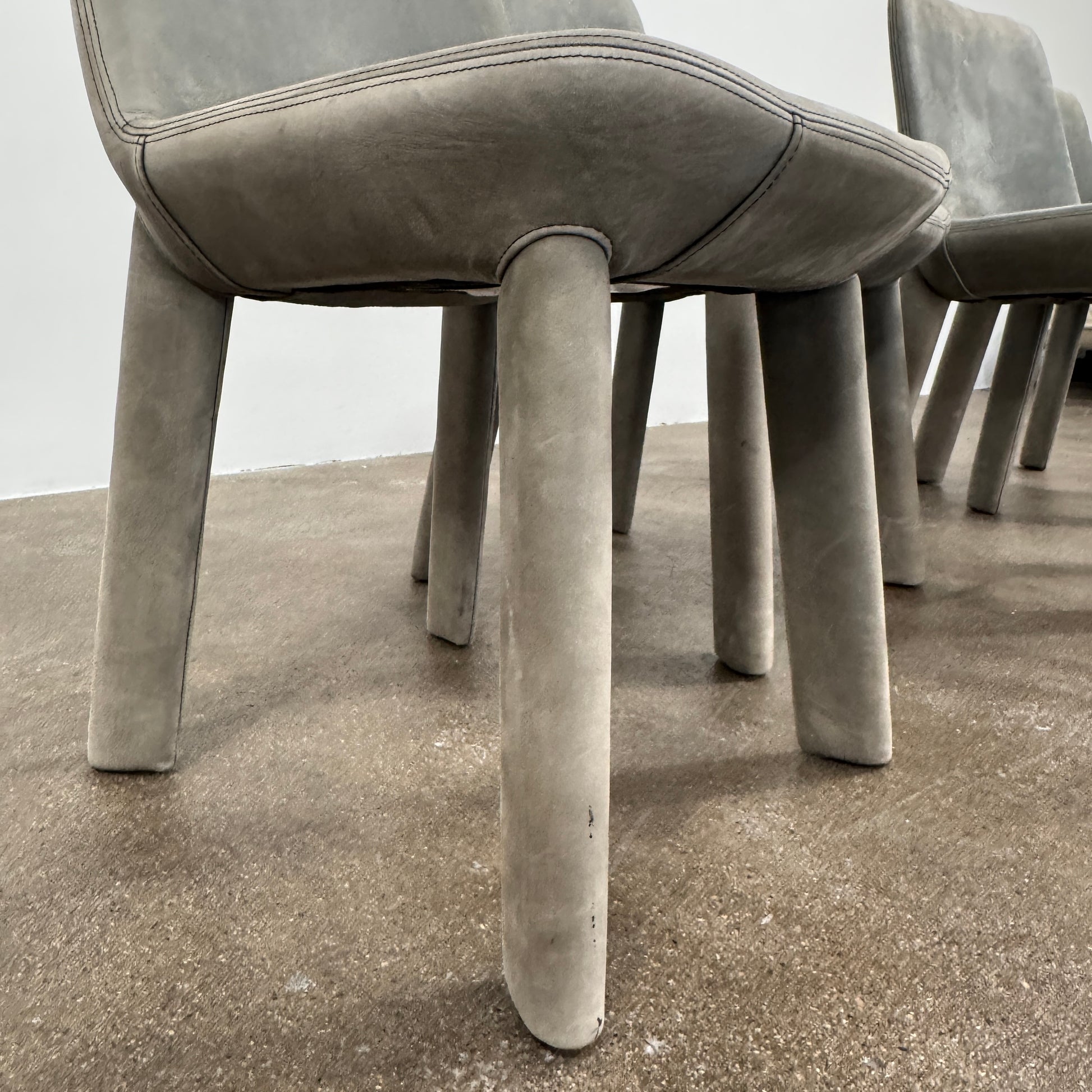 Four Blu Dot Neat Dining Chairs (set of 4, gray) from Blu Dot are lined up against a white wall on a brown concrete floor, highlighting a minimalist and tidy atmosphere.