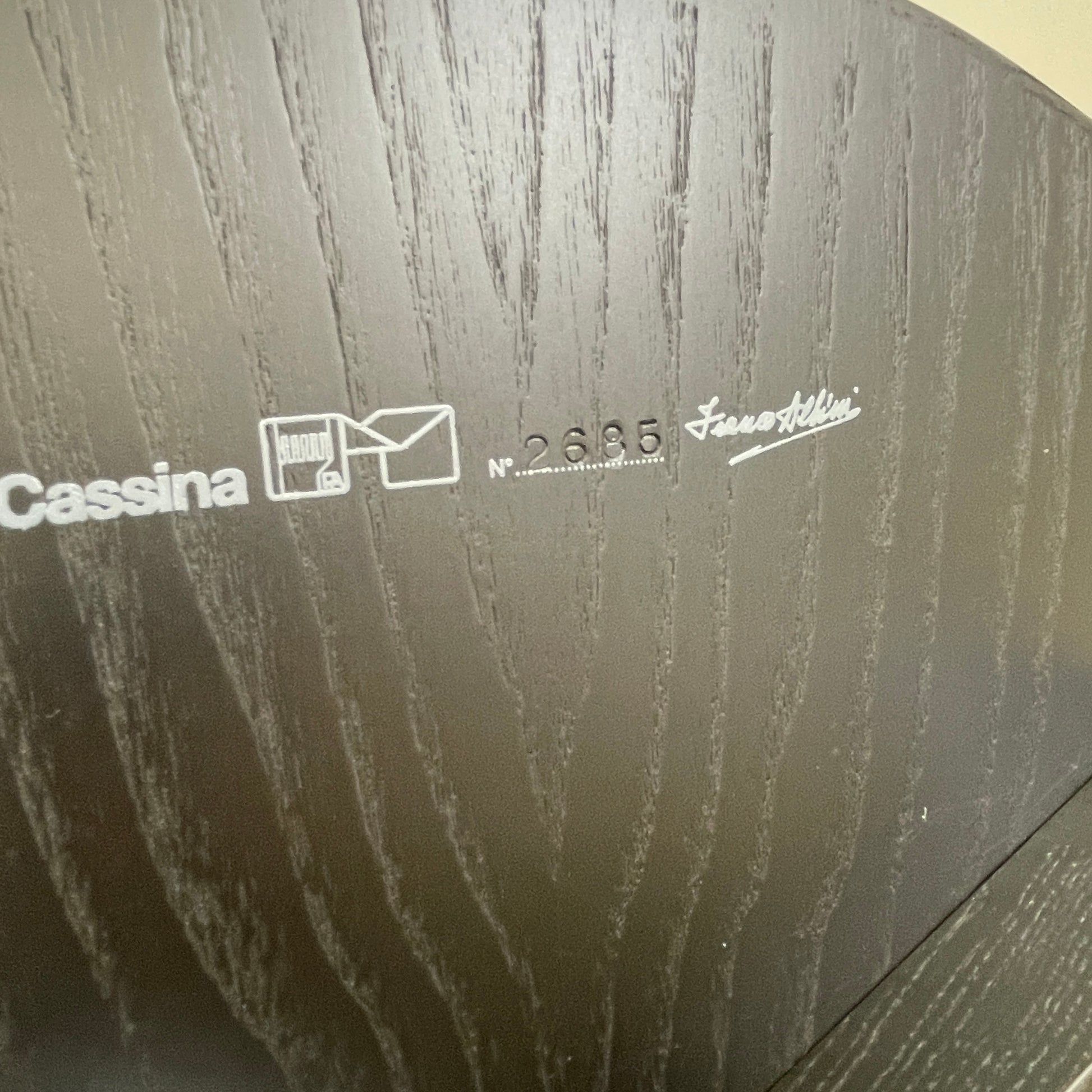 The Cassina Cicognino Side Table by Cassina is black and modern, featuring a round top, three legs, and a vertical handle-like design.