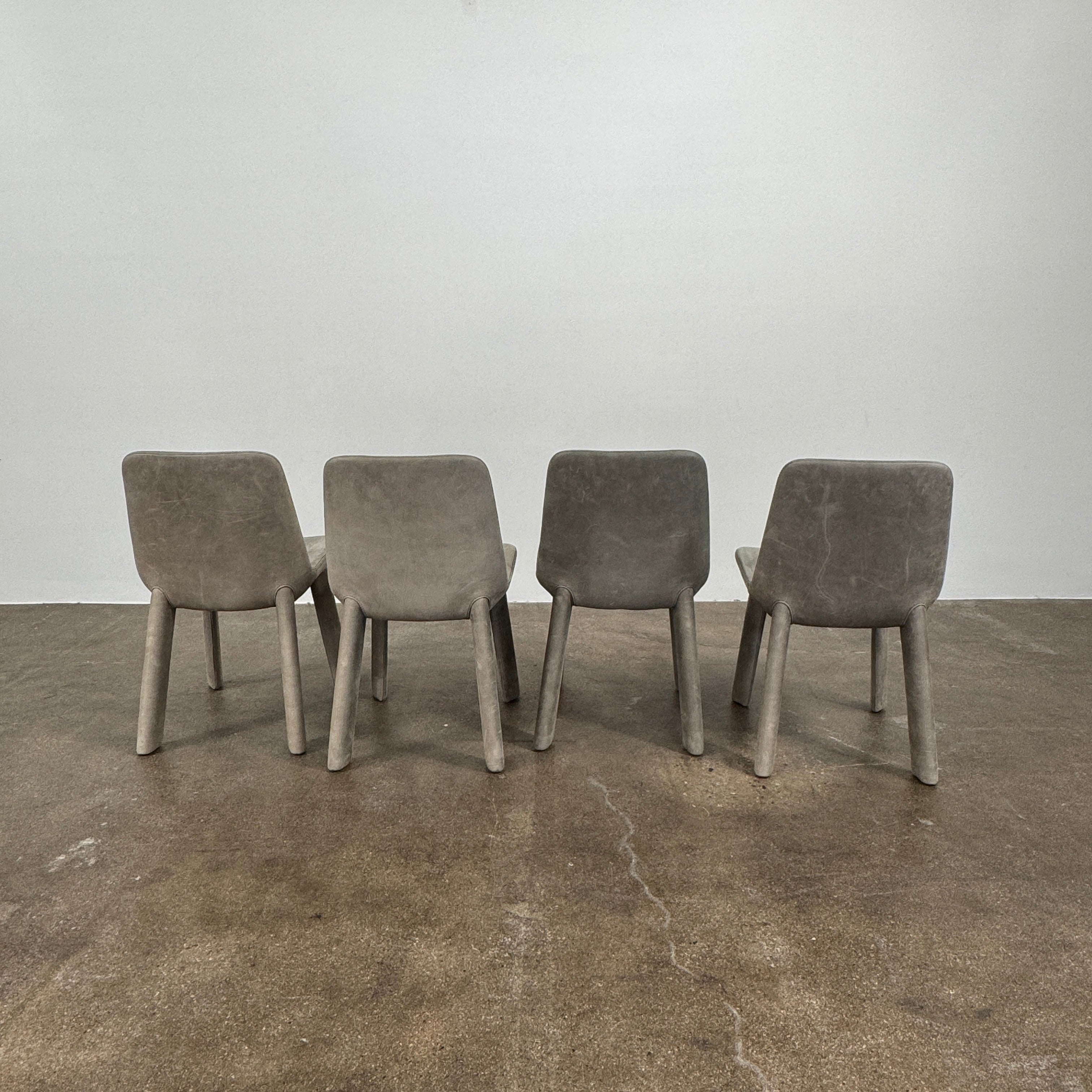 Four Blu Dot Neat Dining Chairs (set of 4, gray) from Blu Dot are lined up against a white wall on a brown concrete floor, highlighting a minimalist and tidy atmosphere.