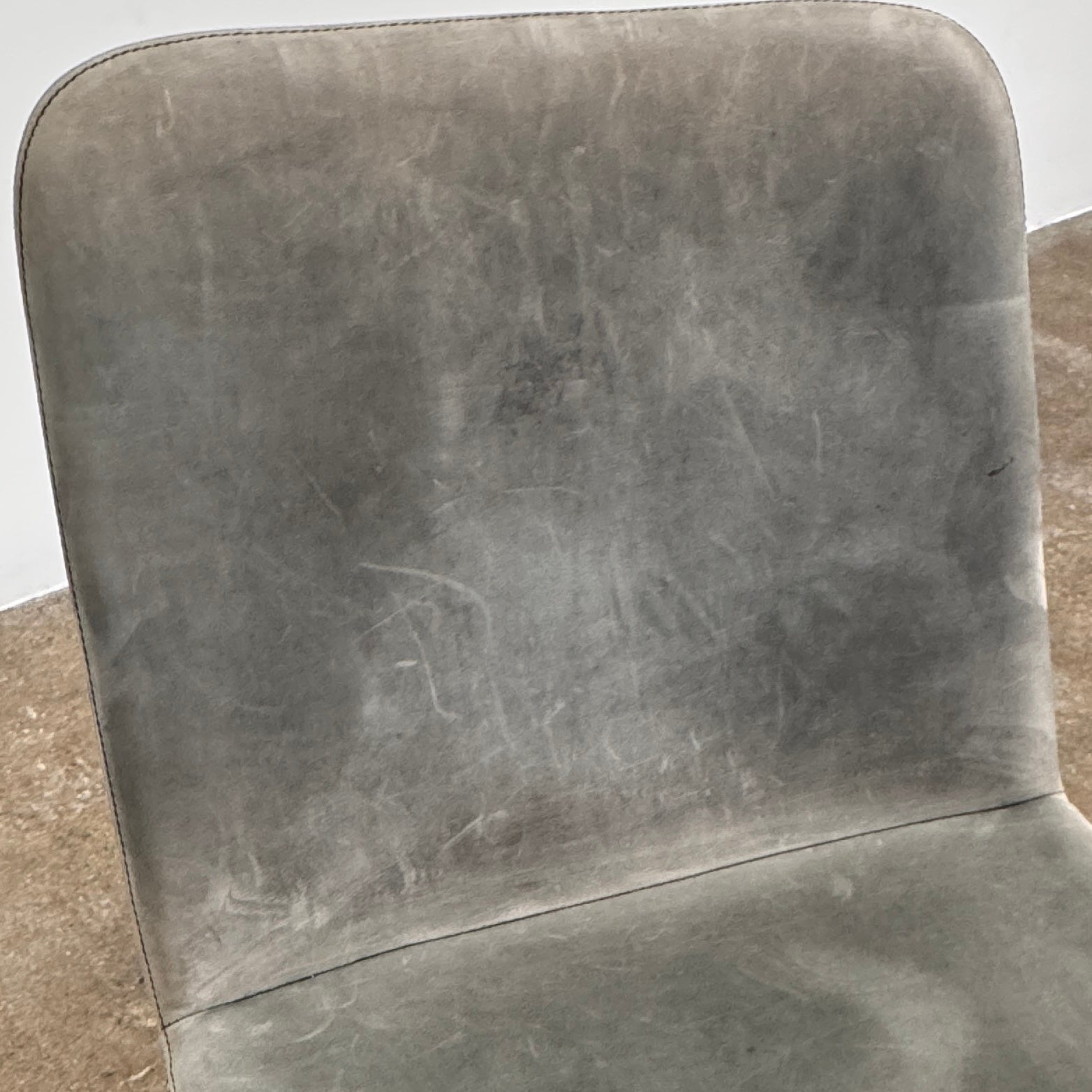 Four Blu Dot Neat Dining Chairs (set of 4, gray) from Blu Dot are lined up against a white wall on a brown concrete floor, highlighting a minimalist and tidy atmosphere.