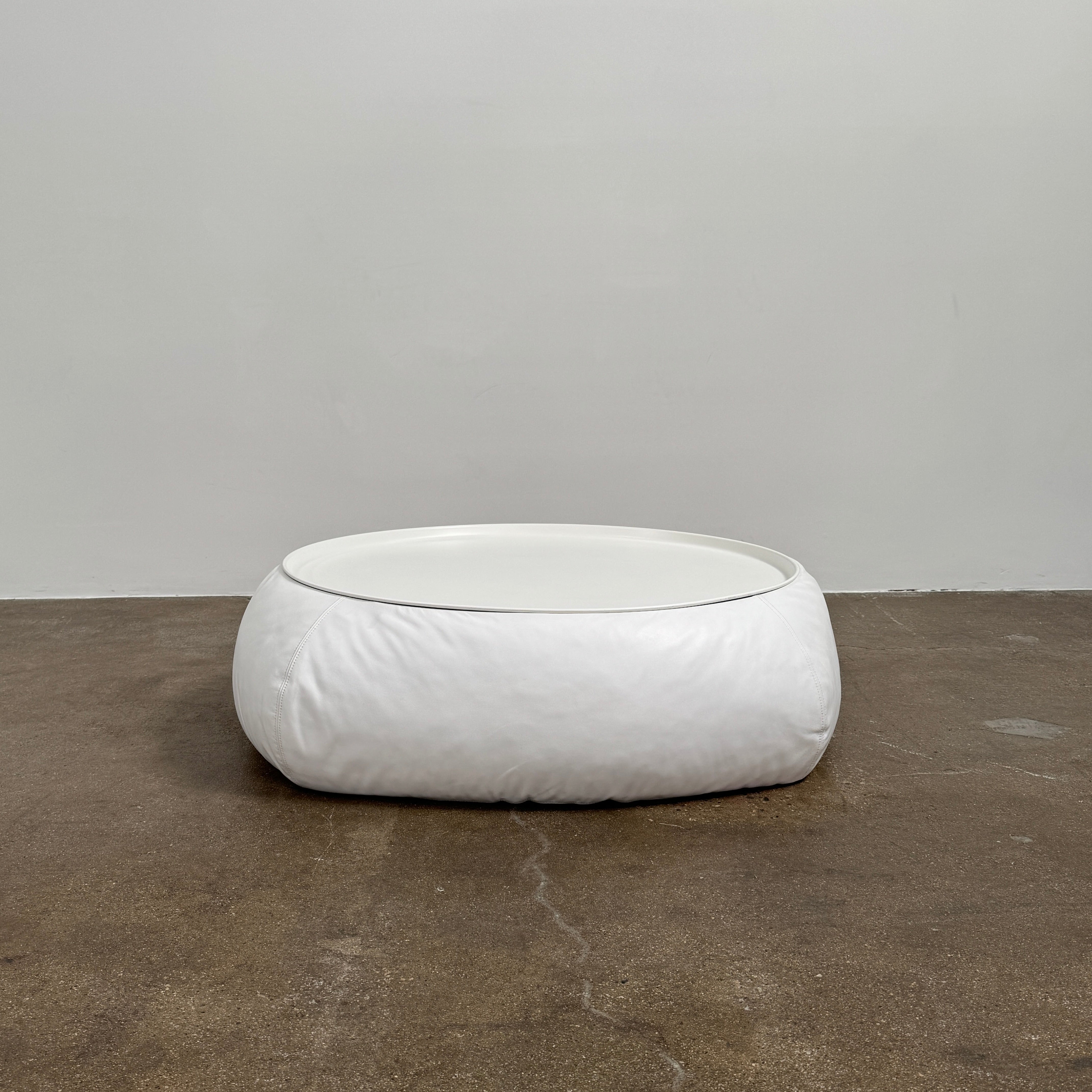 The B&B Italia Lady Fat Coffee Table by B&B Italia, a low, round table with a flat white top inspired by Patricia Urquiola’s design, sits on a plain brown floor against a light gray wall.